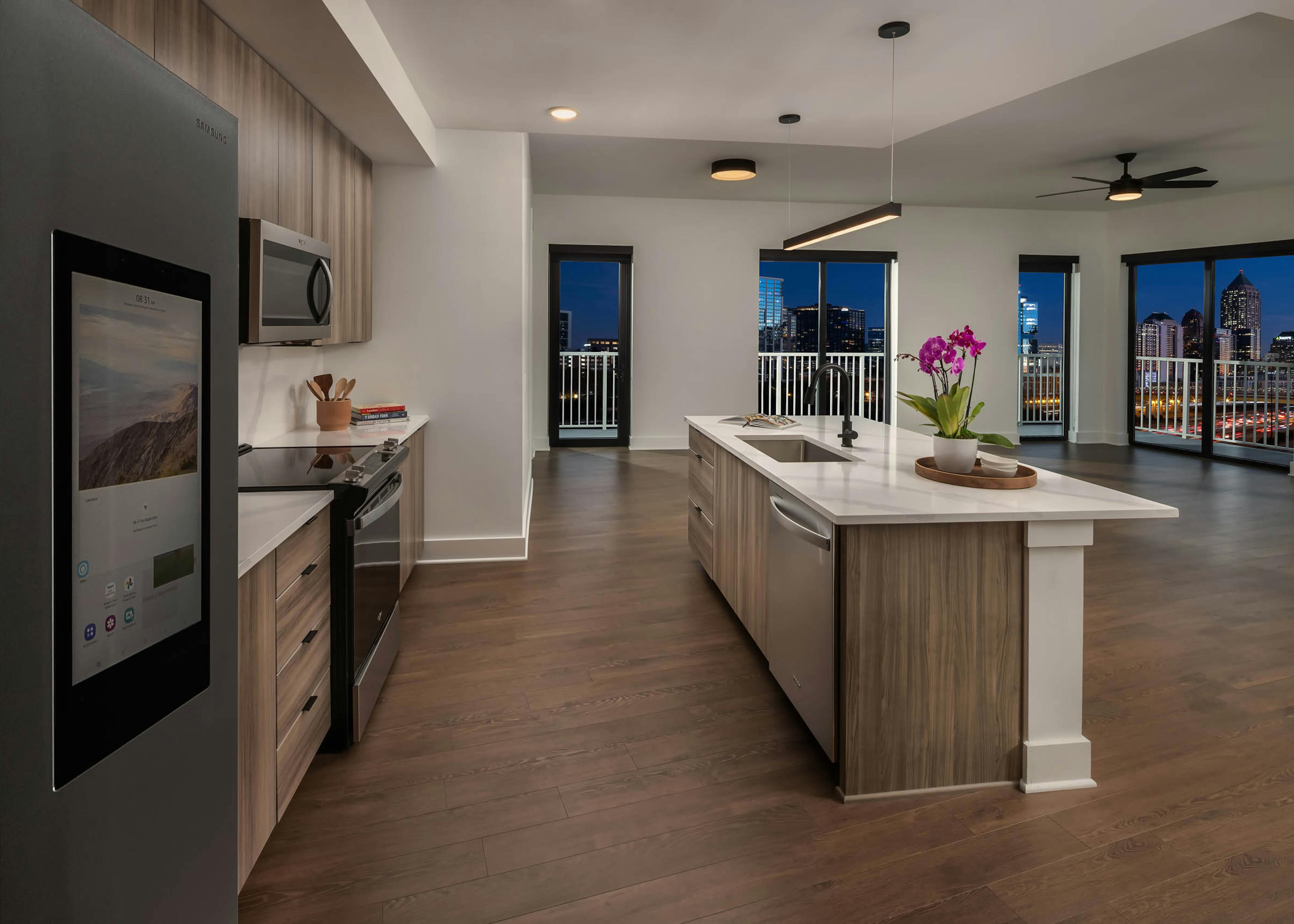 Night view of island kitchen and living area at AMLI Atlantic Station with stainless steel appliances wood cabinets and white countertops