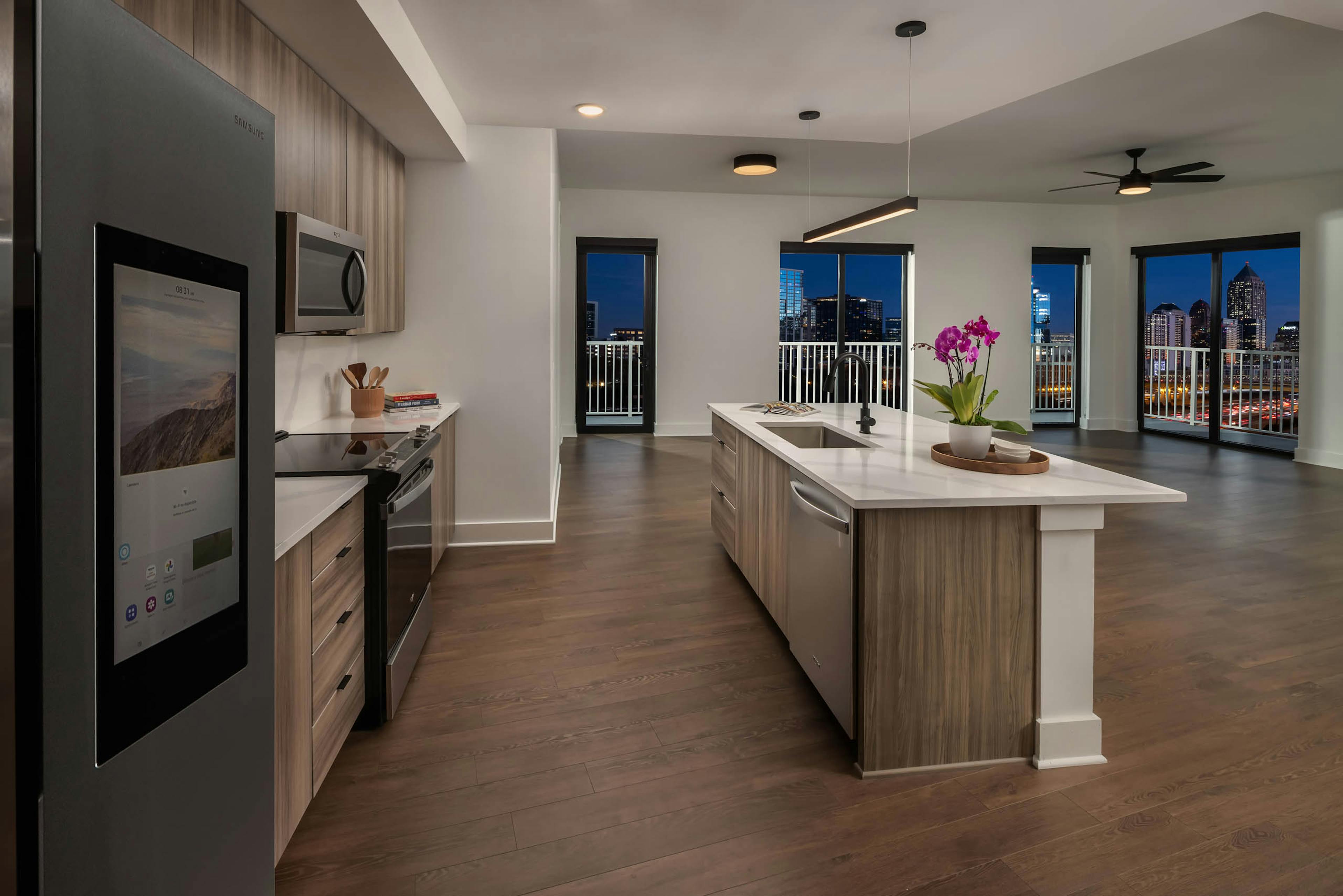 Night view of island kitchen and living area at AMLI Atlantic Station with stainless steel appliances wood cabinets and white countertops