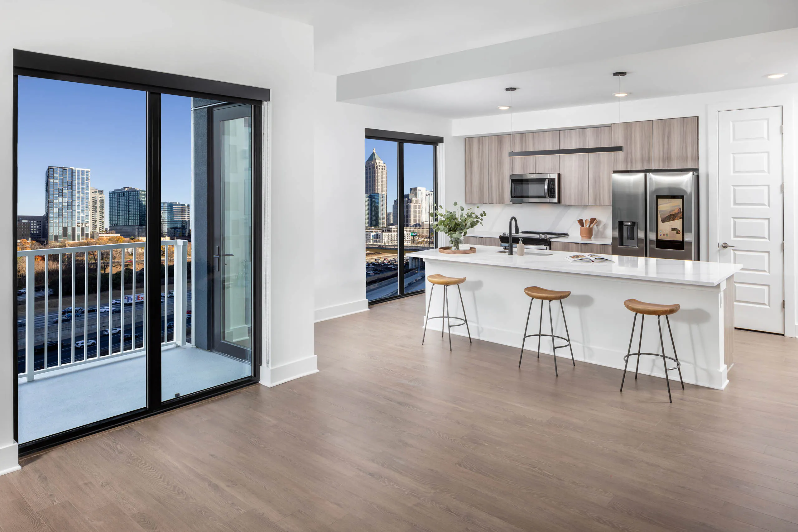 AMLI Atlantic Station apartment island kitchen, living room and balcony with wooden stools and flooring and modern appliances.
