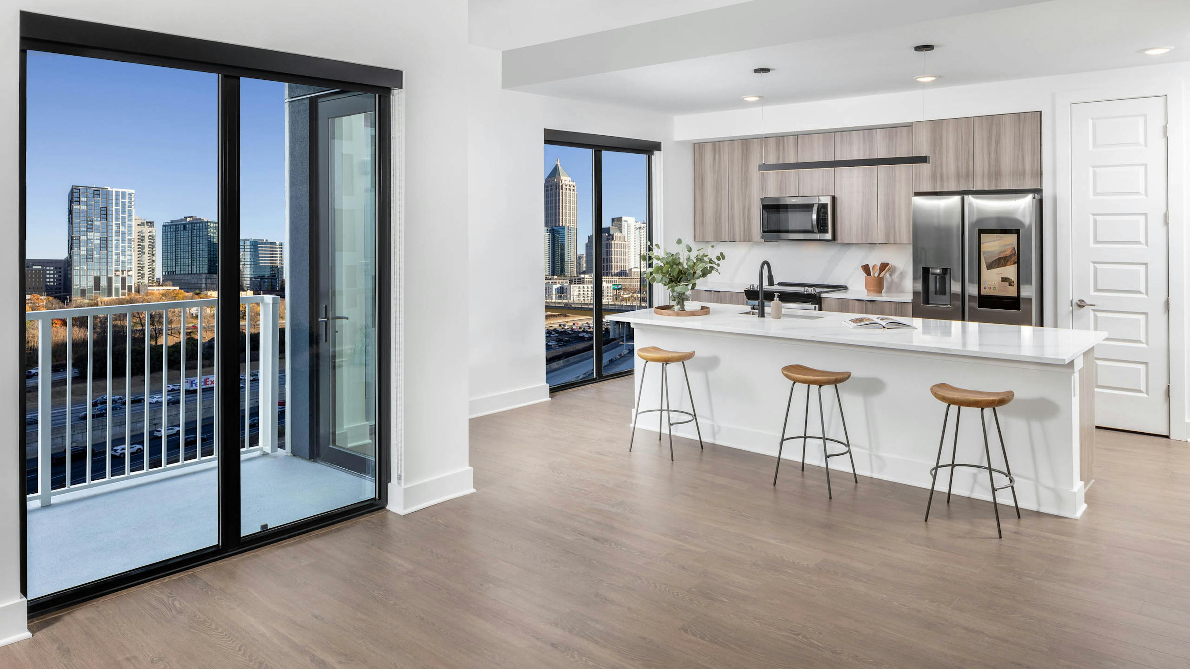 AMLI Atlantic Station apartment island kitchen, living room and balcony with wooden stools and flooring and modern appliances.