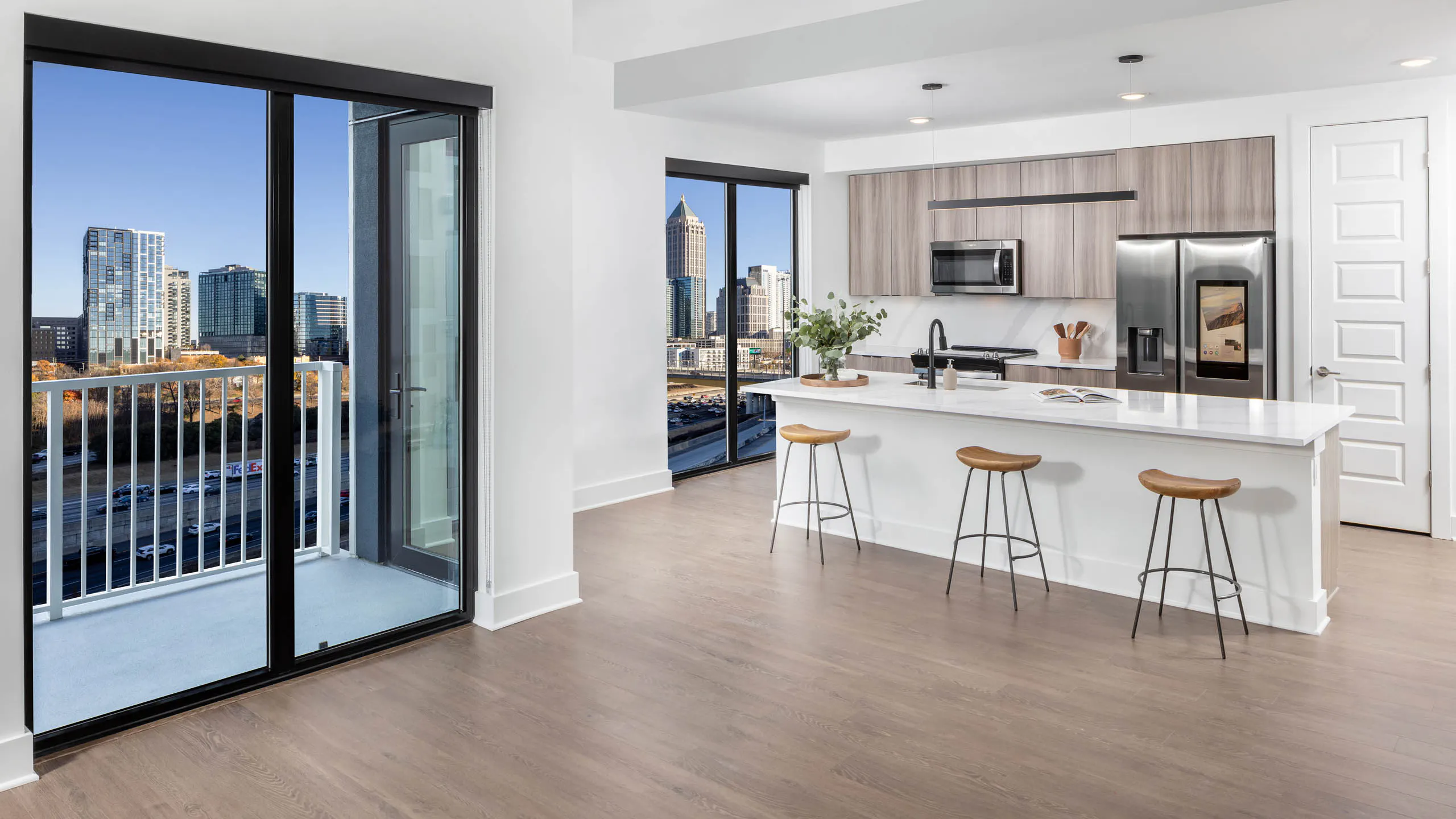 AMLI Atlantic Station apartment island kitchen, living room and balcony with wooden stools and flooring and modern appliances.