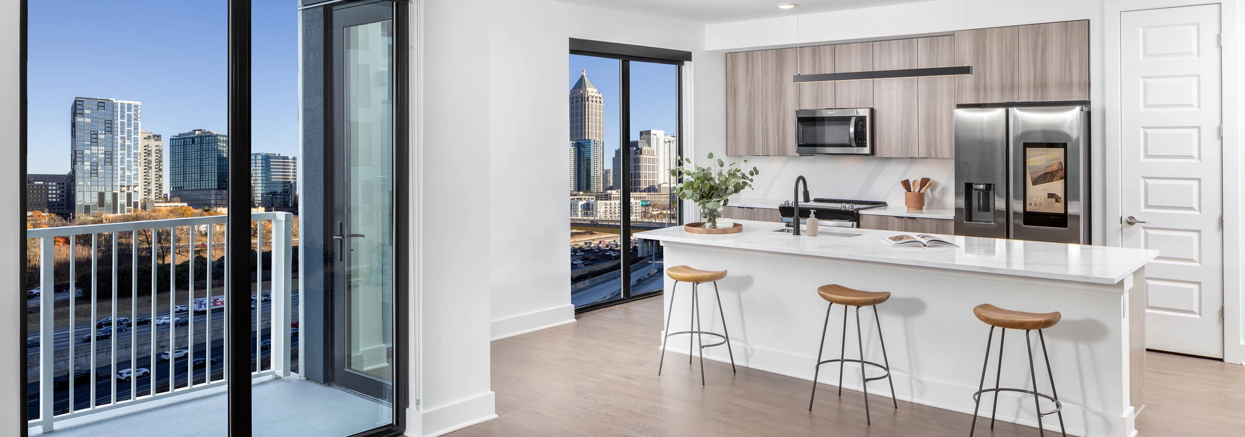 AMLI Atlantic Station apartment island kitchen, living room and balcony with wooden stools and flooring and modern appliances.