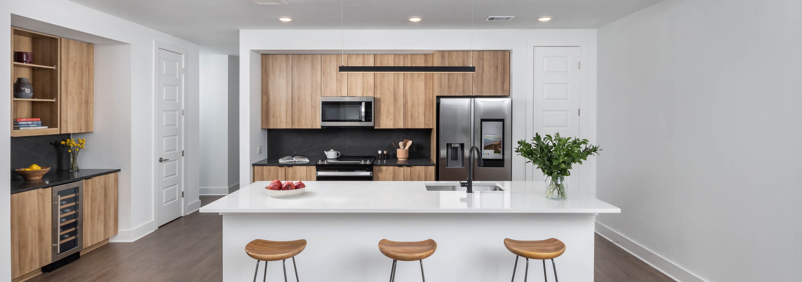 Entryway showing a kitchen and bar area at AMLI Atlantic Station with black and white counters, wood cabinets and three bar stools.