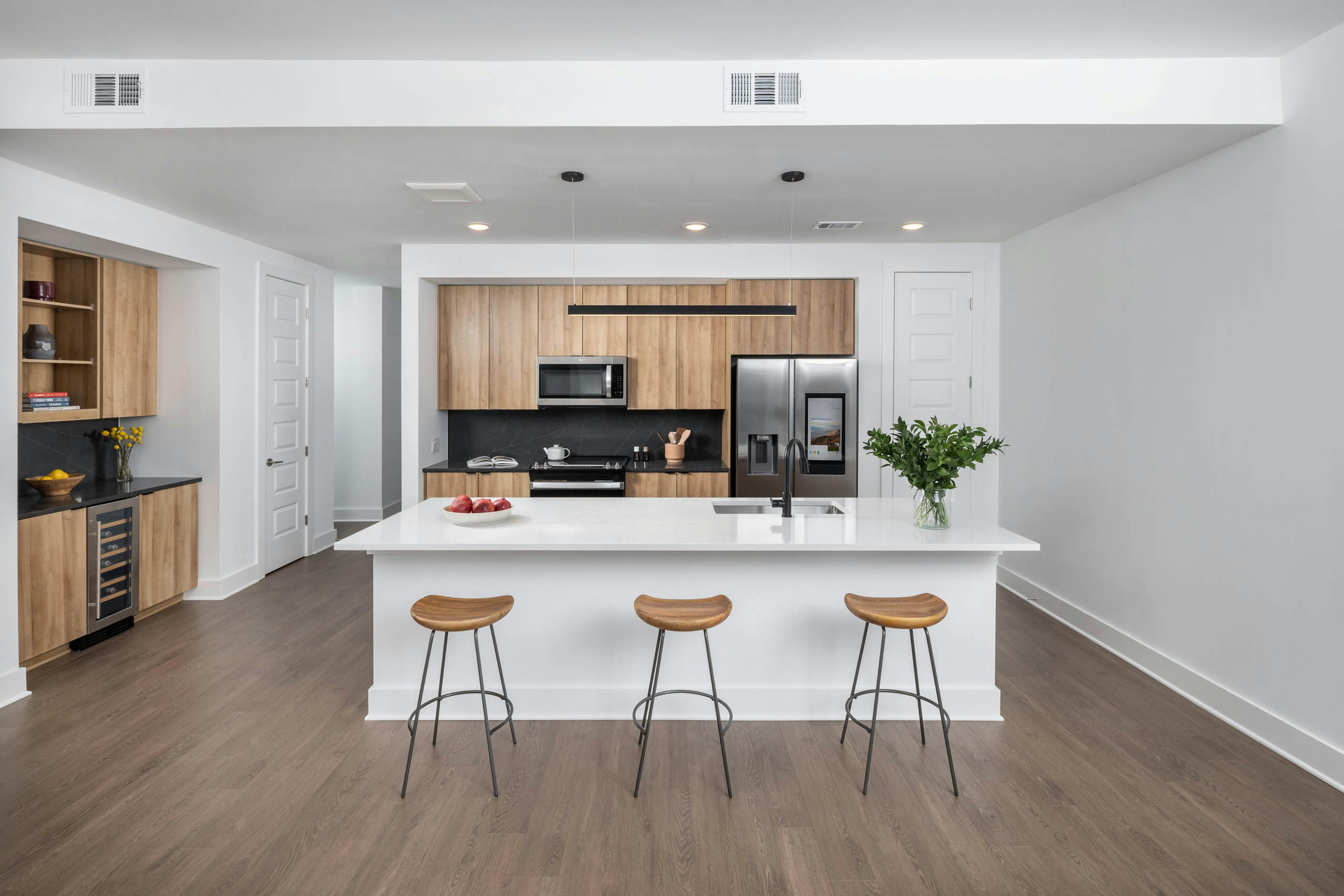 Entryway showing a kitchen and bar area at AMLI Atlantic Station with black and white counters, wood cabinets and three bar stools.