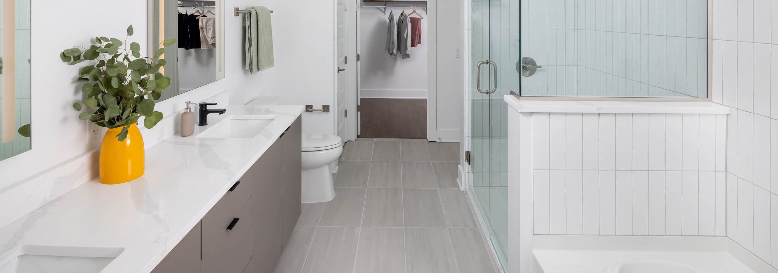 Modern bathroom at AMLI Atlantic Station with tile flooring, double vanity, a glass shower, bathtub, and view to the closet