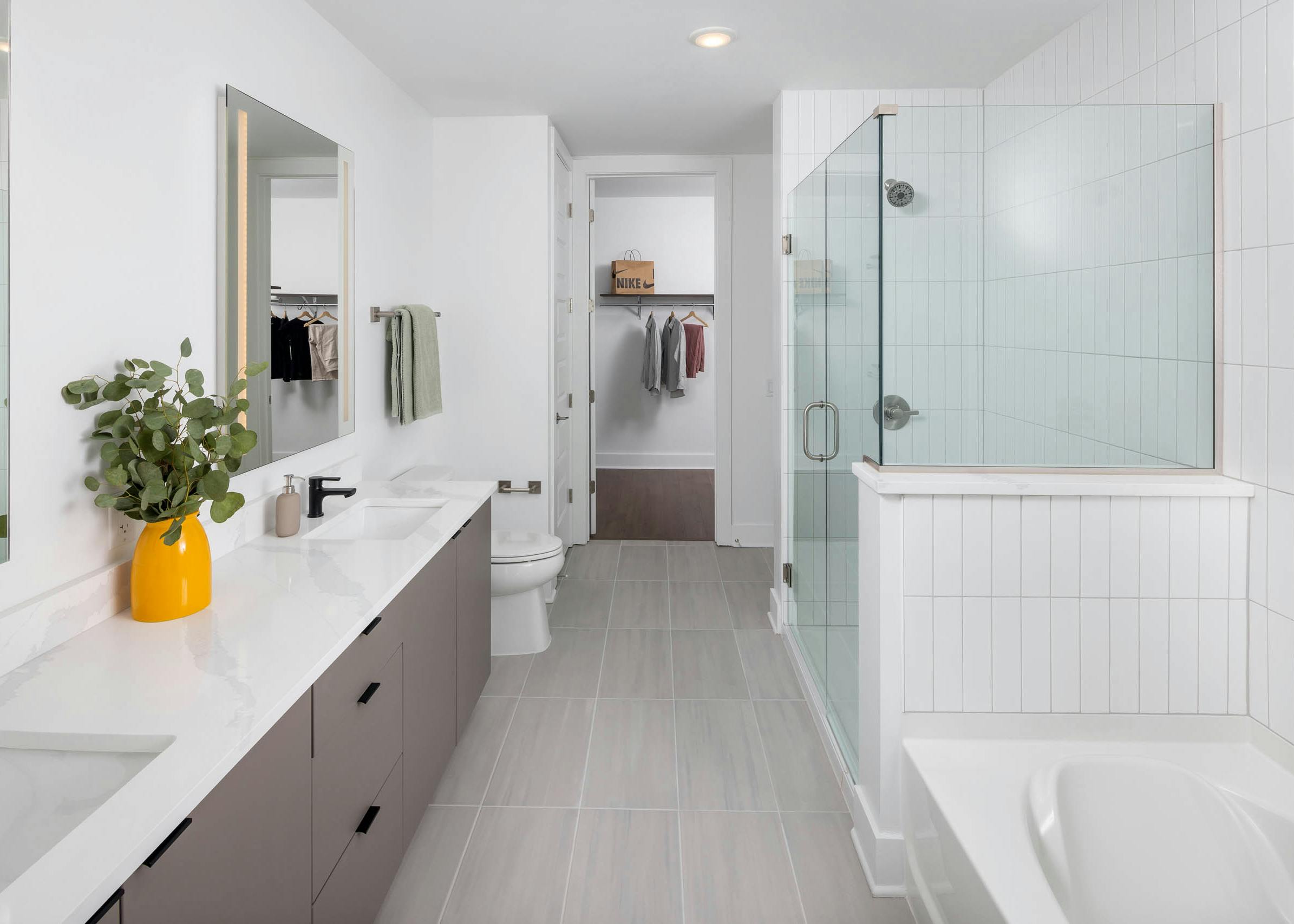 Modern bathroom at AMLI Atlantic Station with tile flooring, double vanity, a glass shower, bathtub, and view to the closet