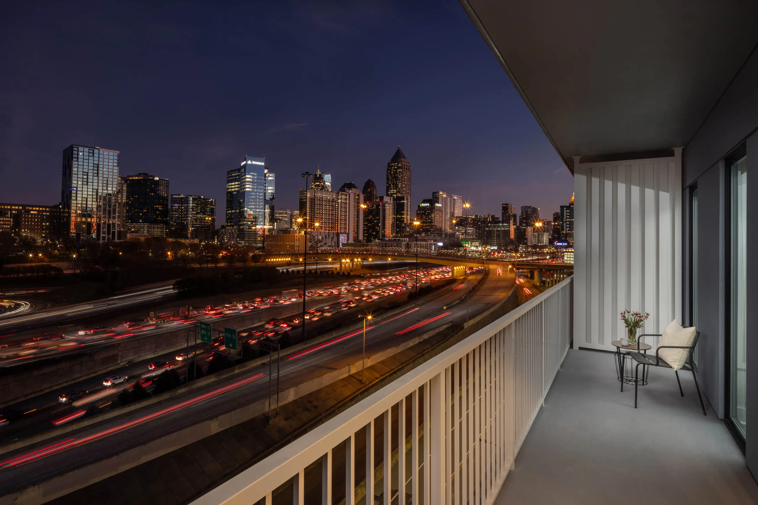 Long balcony overlooking a night view of a cityscape at AMLI Atlantic Station with a chair and side table/