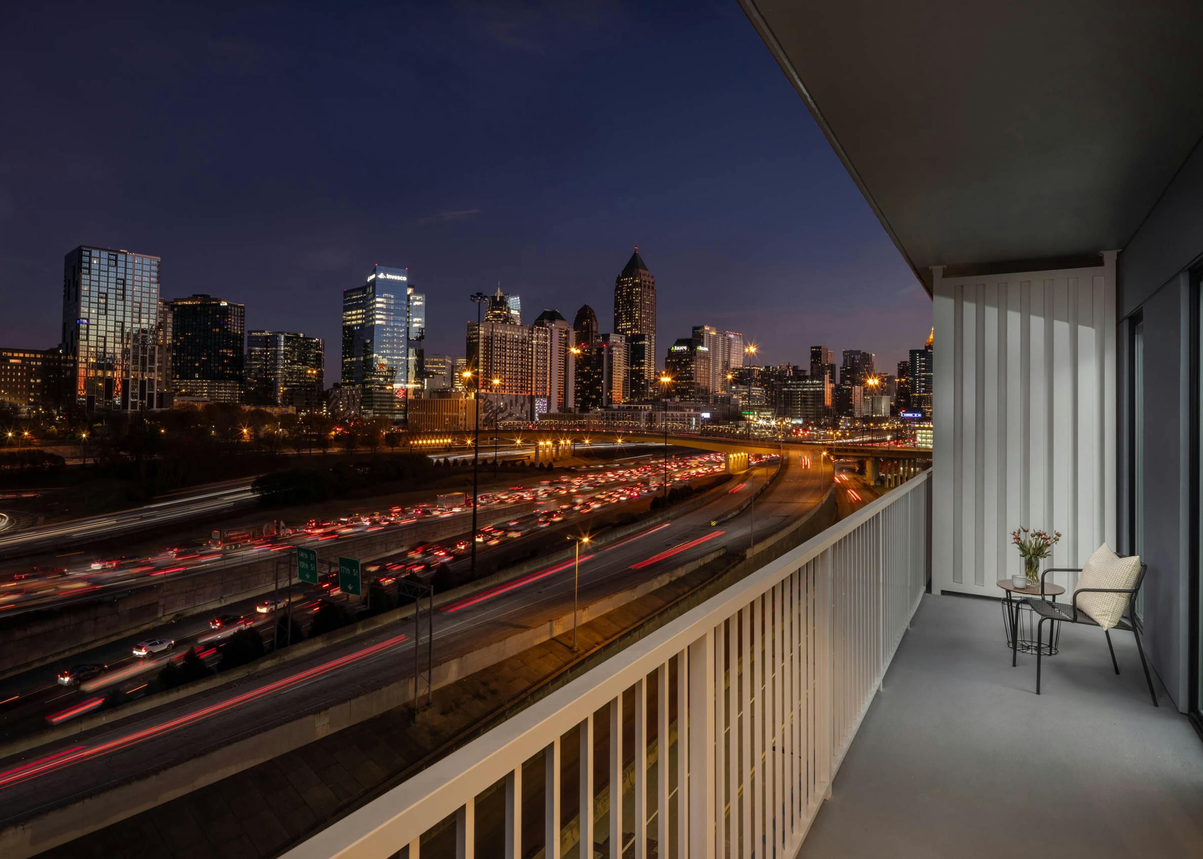 Long balcony overlooking a night view of a cityscape at AMLI Atlantic Station with a chair and side table/