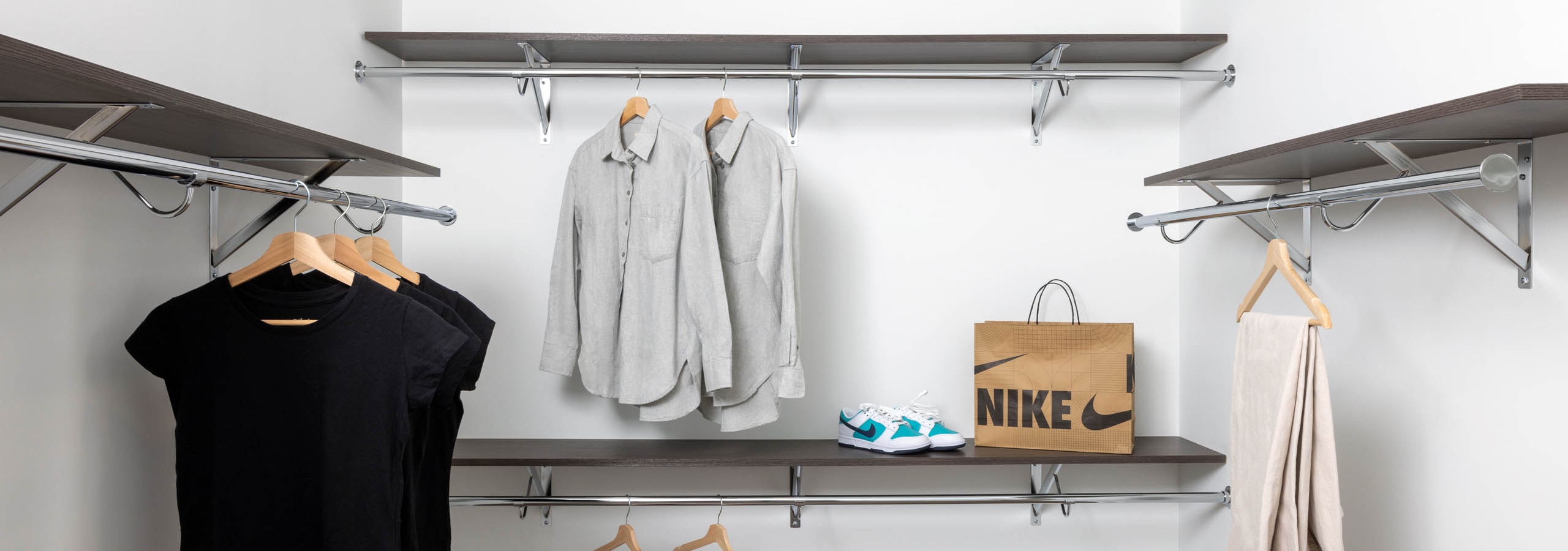 Large walk in closet at AMLI Atlantic Station with chrome rods, wood shelving with sneakers, shirts and pants arranged on shelves and hangers.