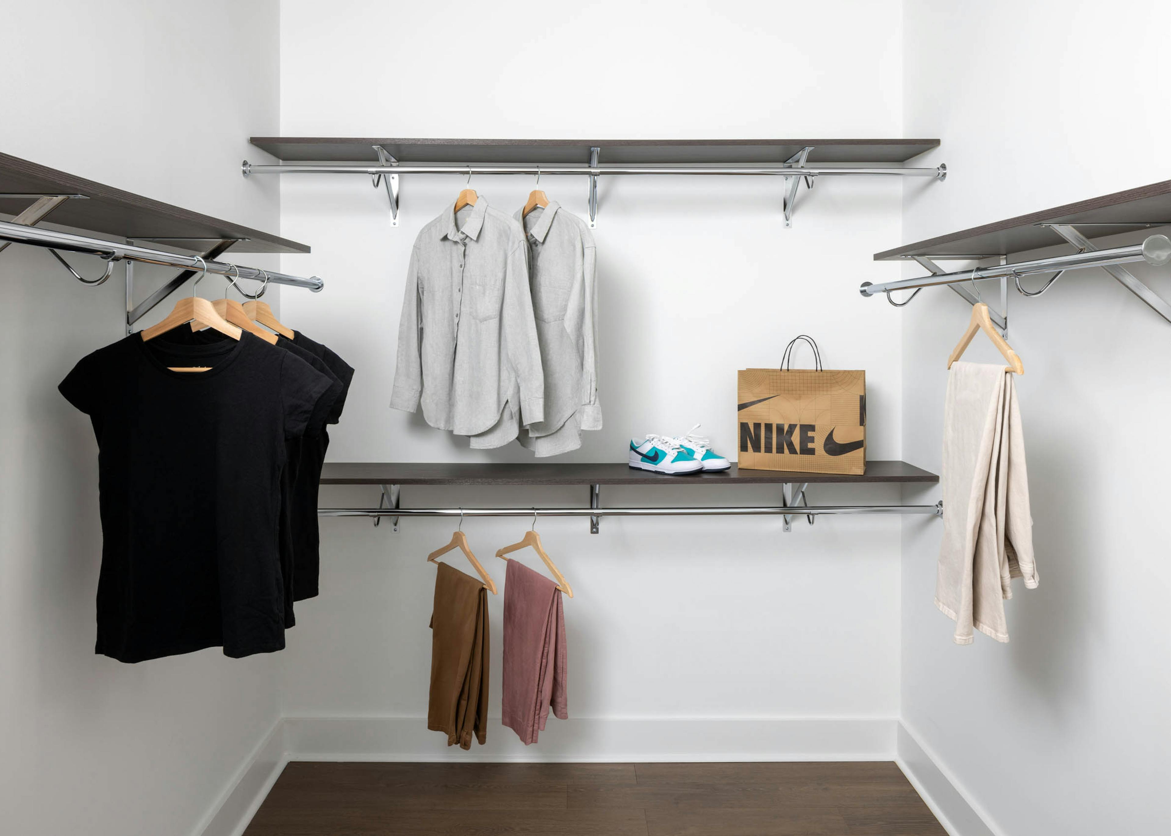 Large walk in closet at AMLI Atlantic Station with chrome rods, wood shelving with sneakers, shirts and pants arranged on shelves and hangers.