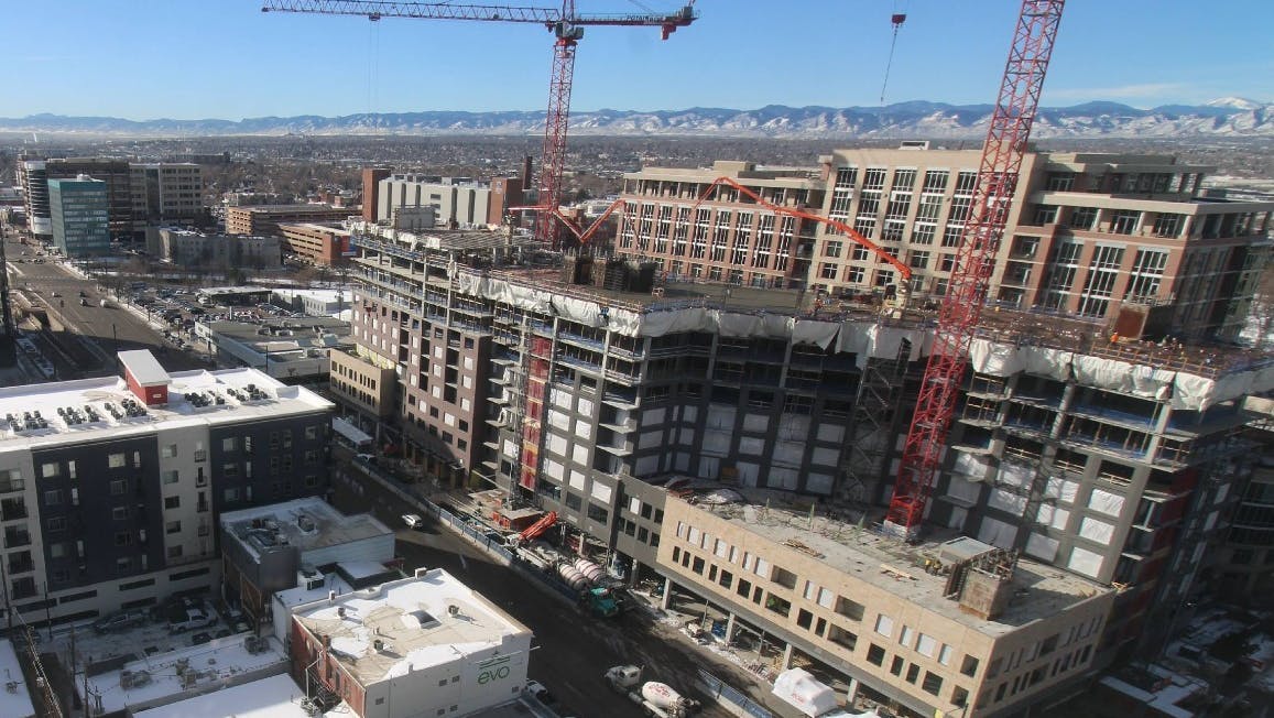 AMLI Golden Triangle apartment building under construction with fifth floor amenity deck being completed and 2 tall orange cranes