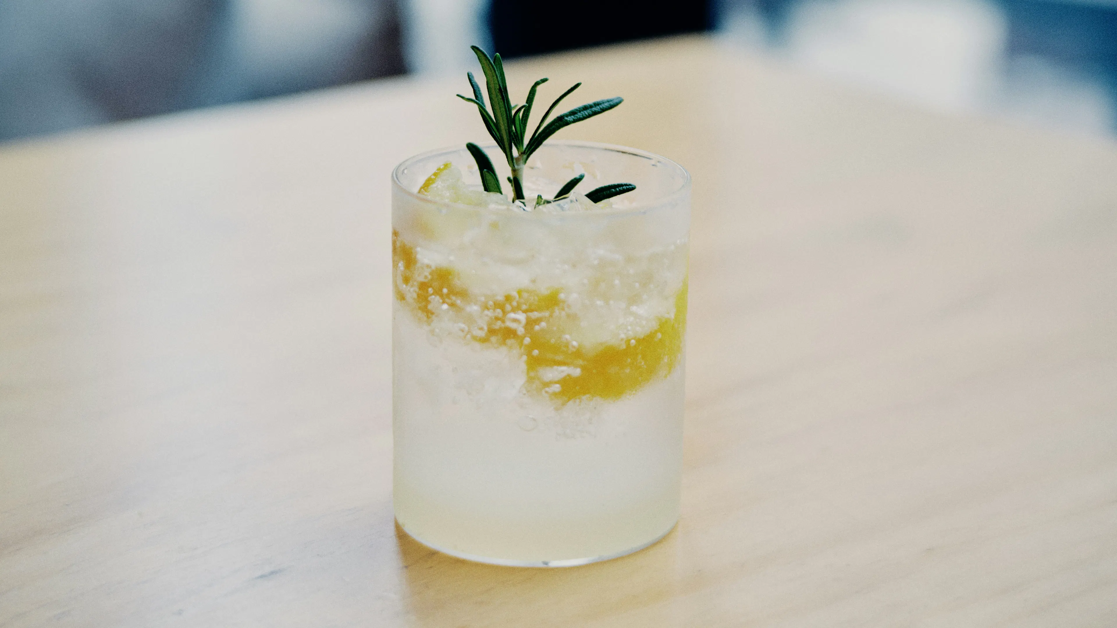 A glass of ice and sparkling water with a slice of lemon and a sprig of rosemary to garnish