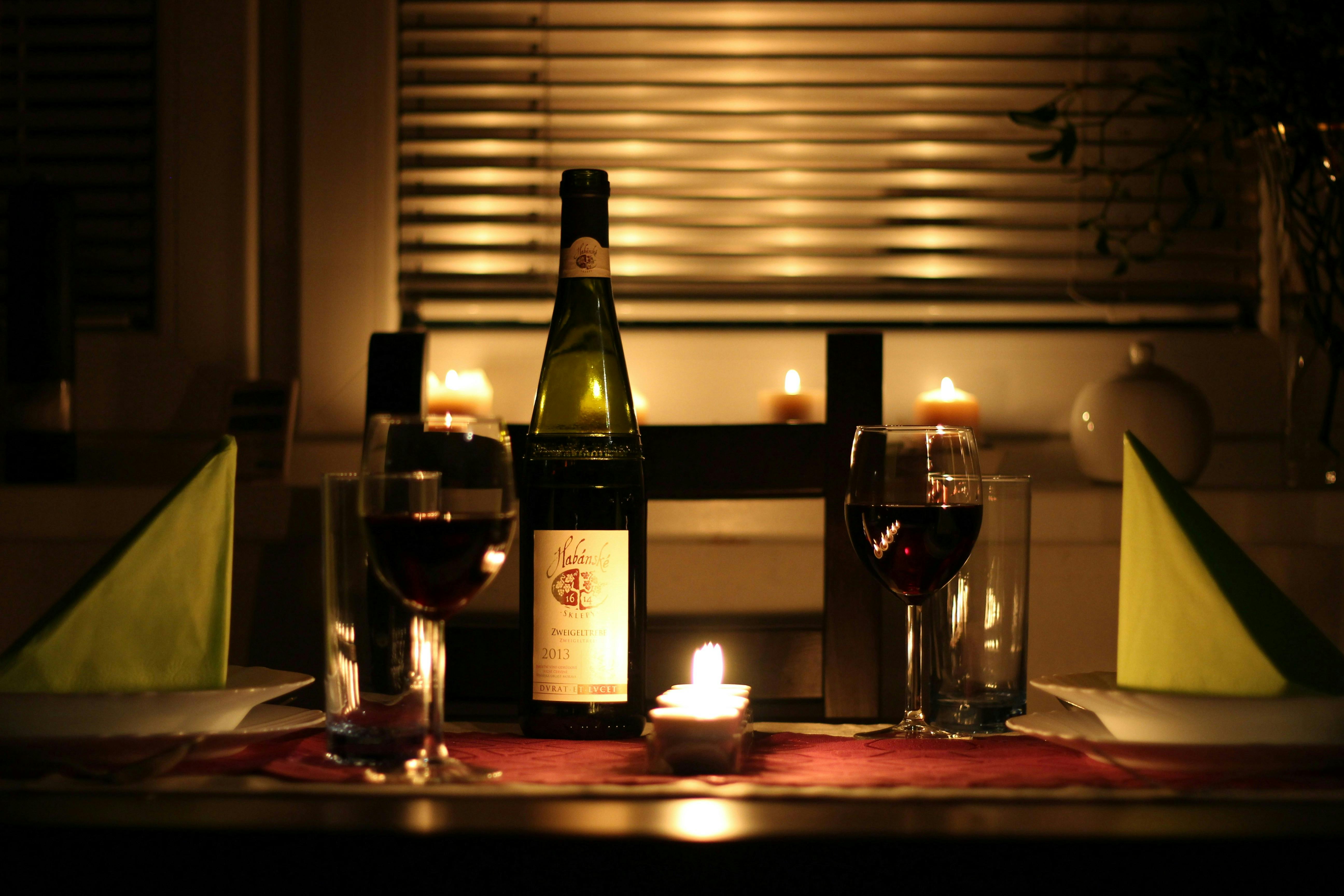 A bottle of red wine on a table with two full wine glasses and a small tea light candle