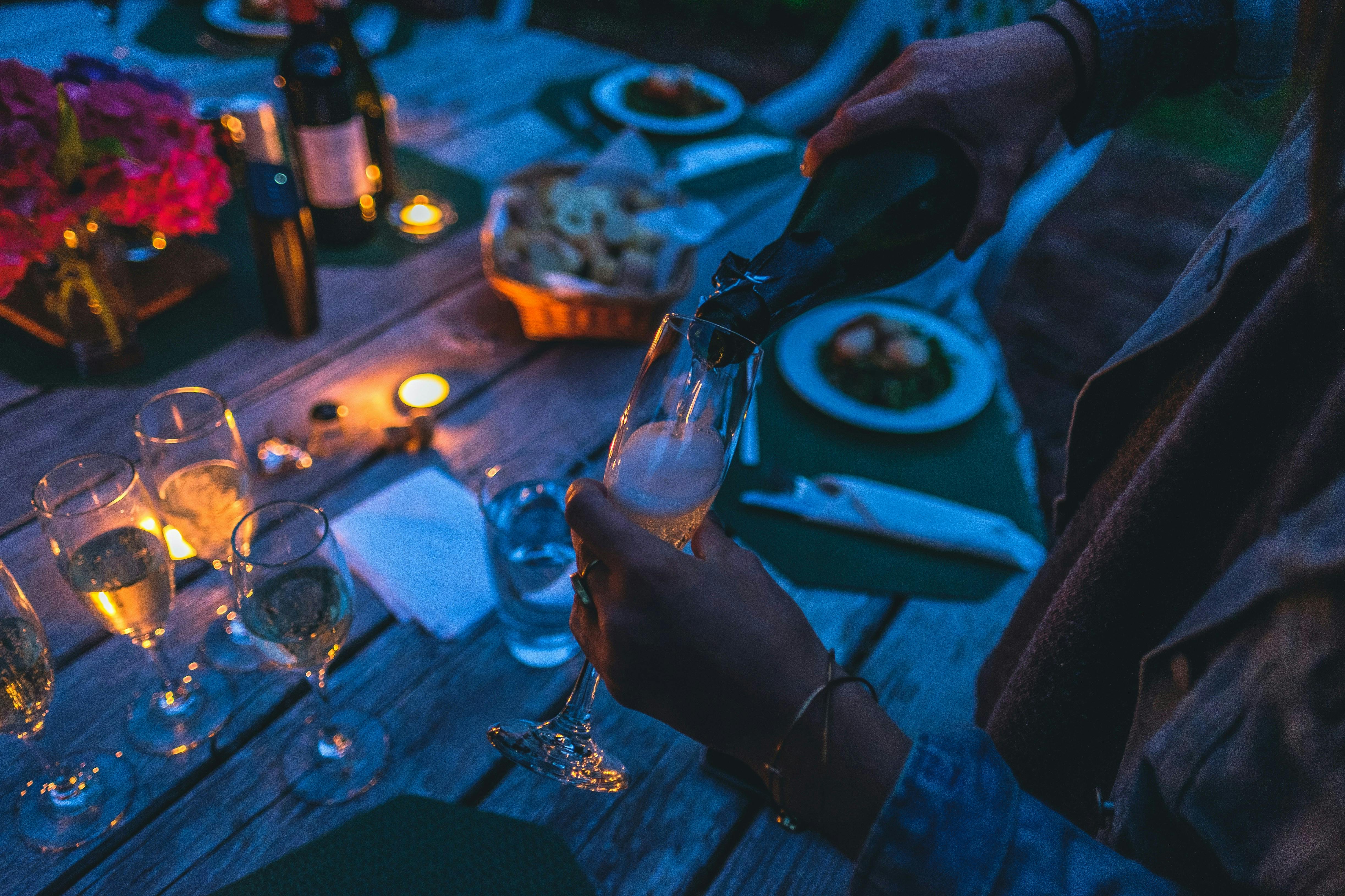 Person pouring wine into glass flute at an outdoor dinner table decorated with candles