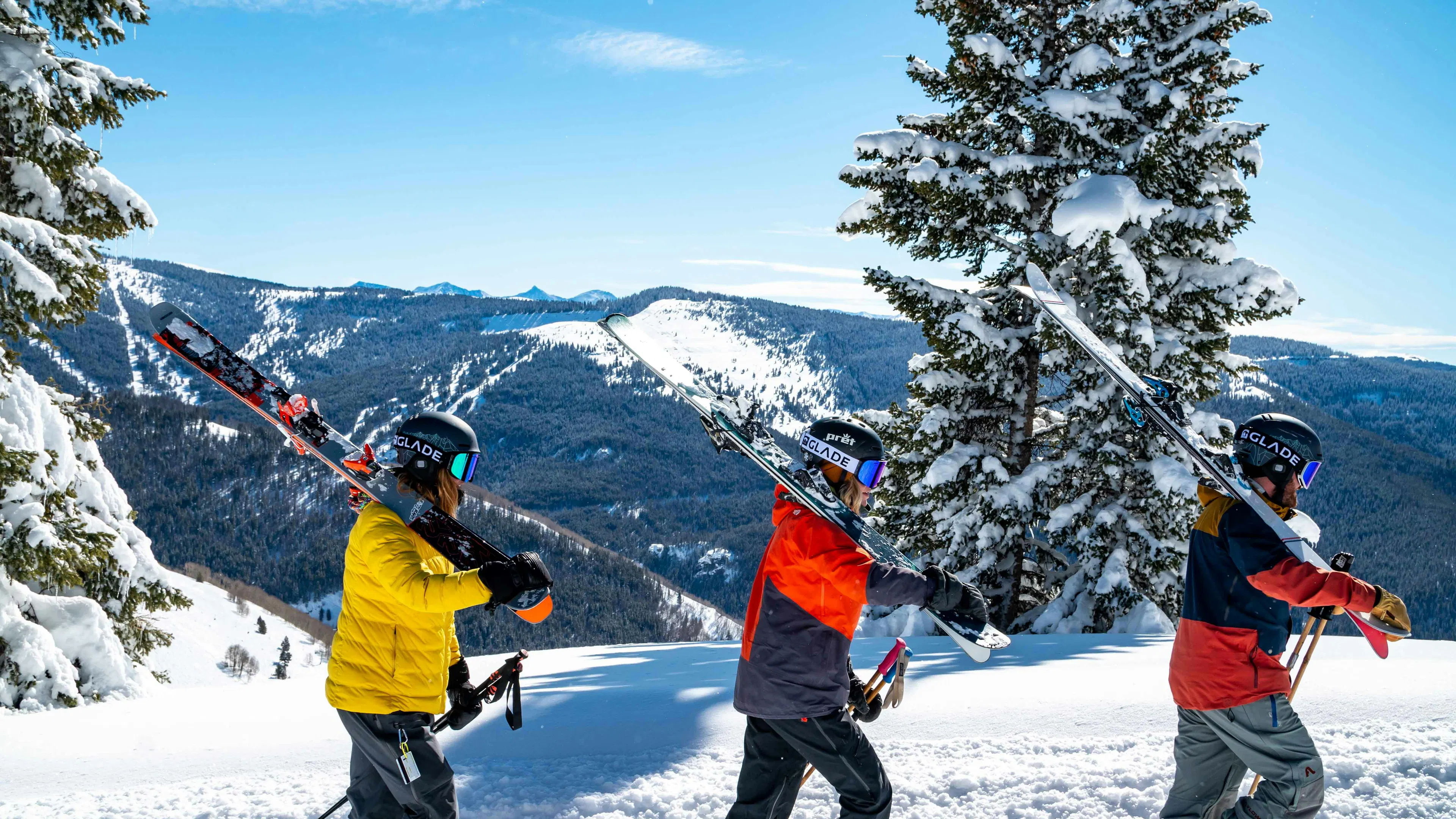 Three skiiers carrying their backcountry skis on a trail up a snowy mountain