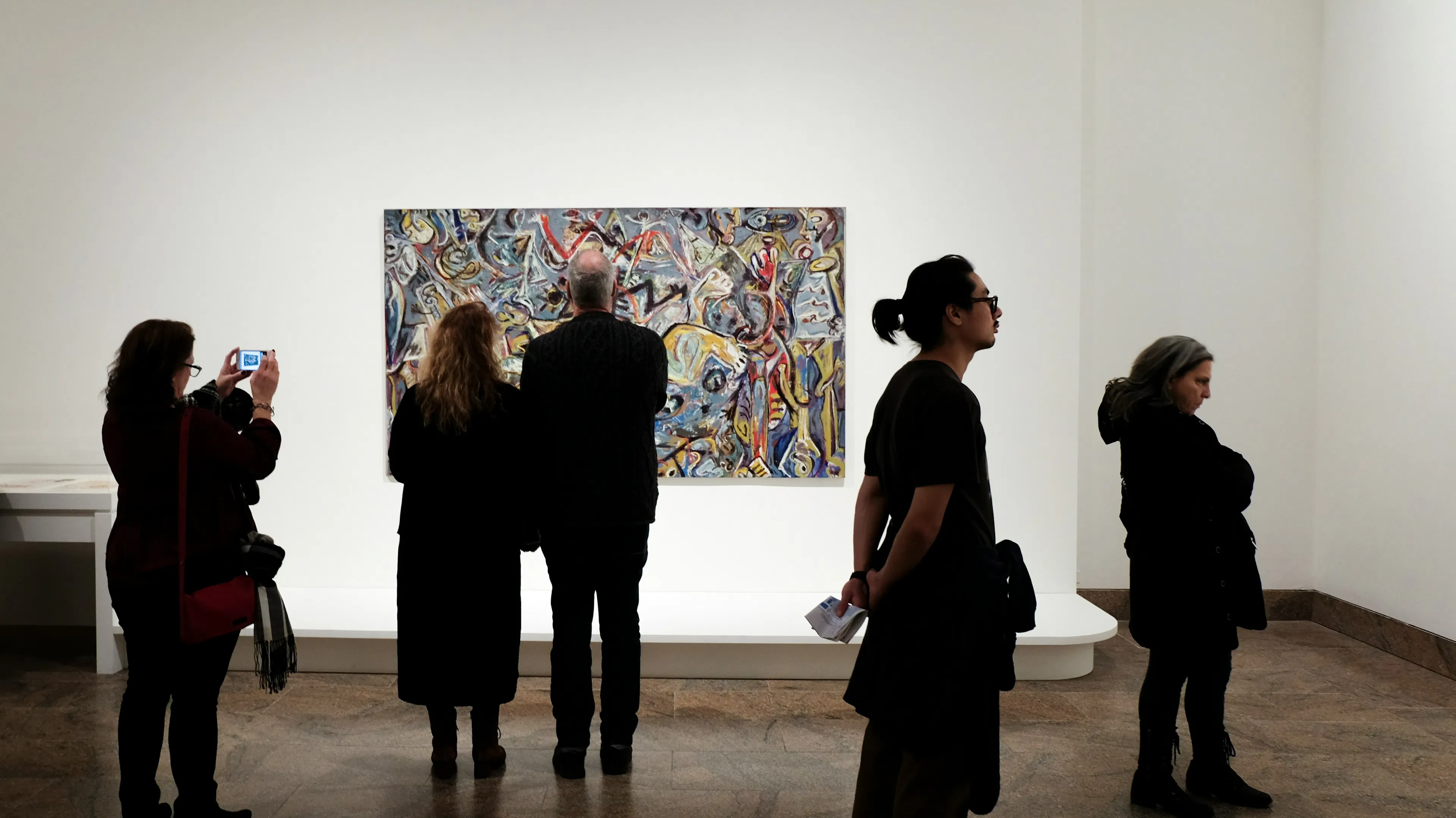 a bright art gallery with a single colorful splatter paint artwork on the wall with people silhouetted in front of it