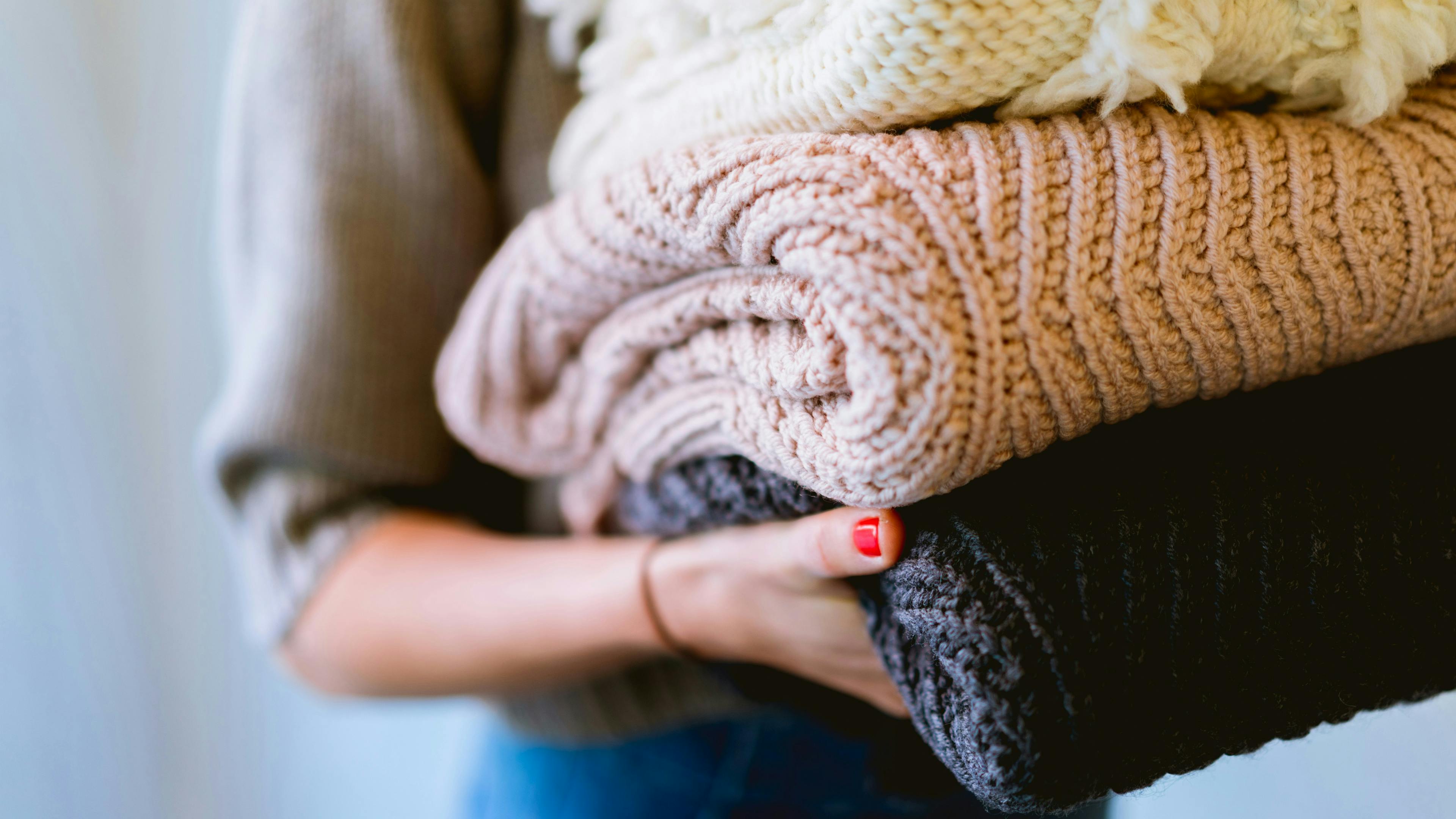 A woman holding three folded knitted sweaters