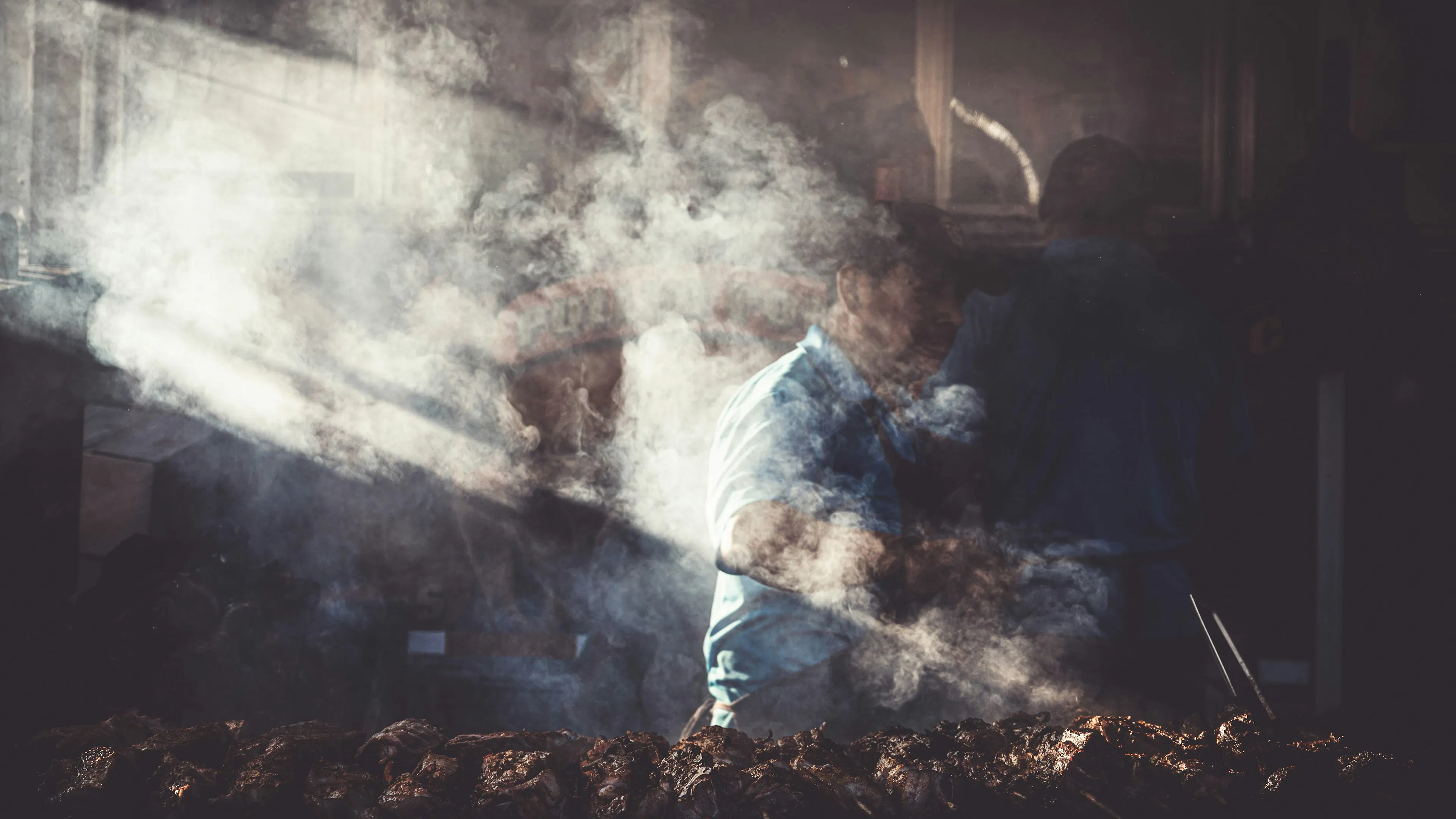 A man almost entirely hidden by smoke from a meat smoker he is using
