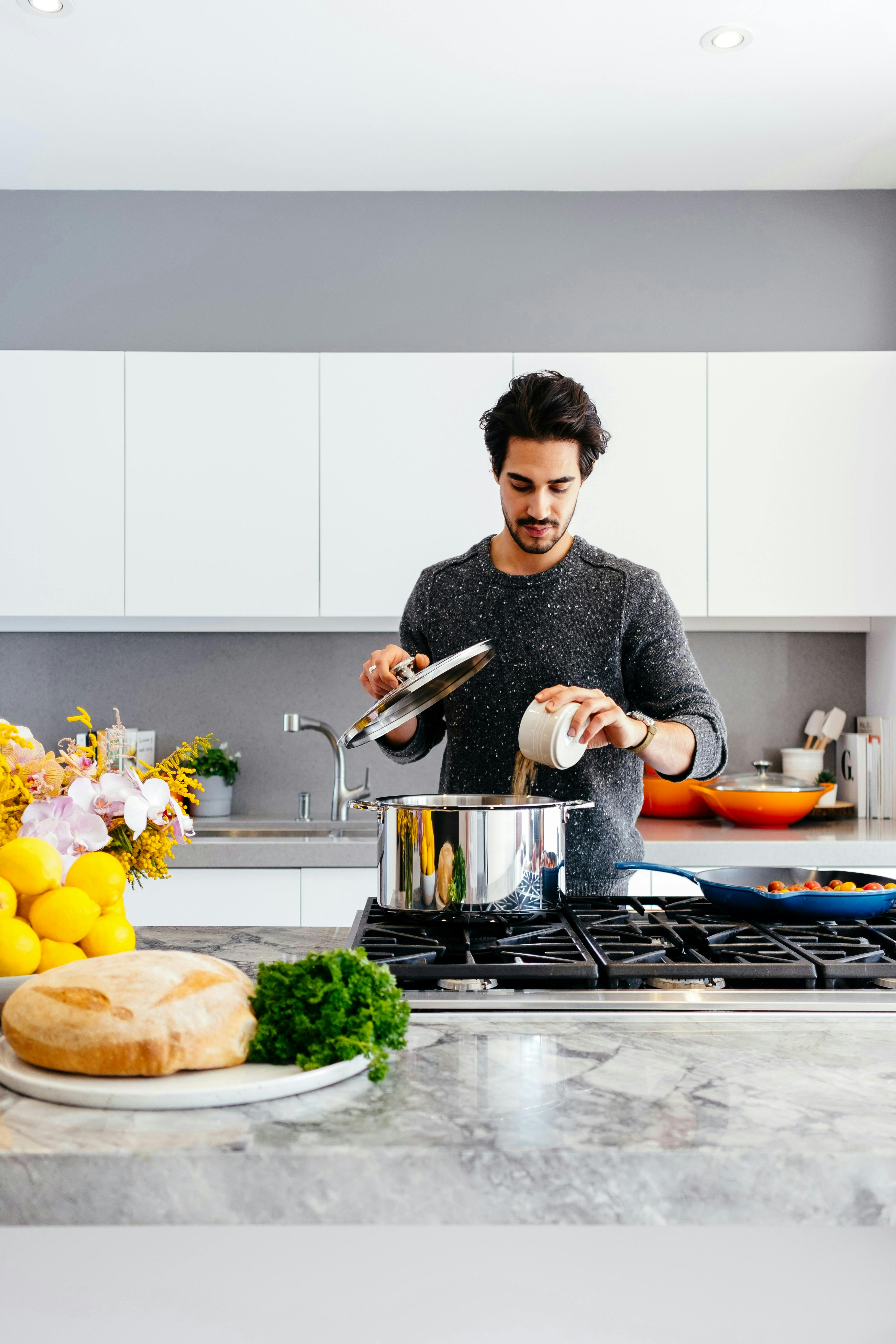 A man pouring lentils into a large steel pot in a clean and bright kitchen