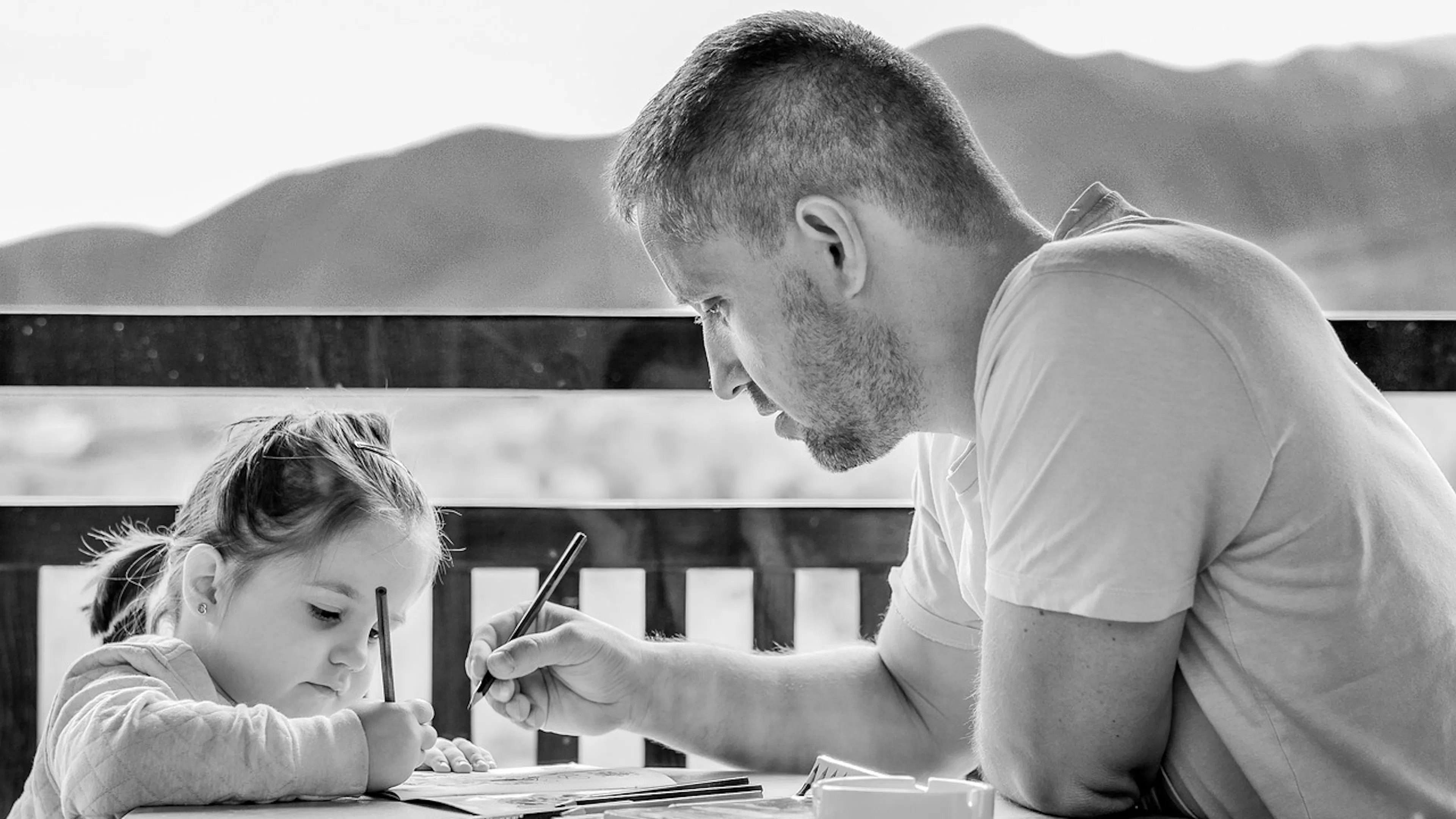 small girl at table with her father drawing pictures by the mountains