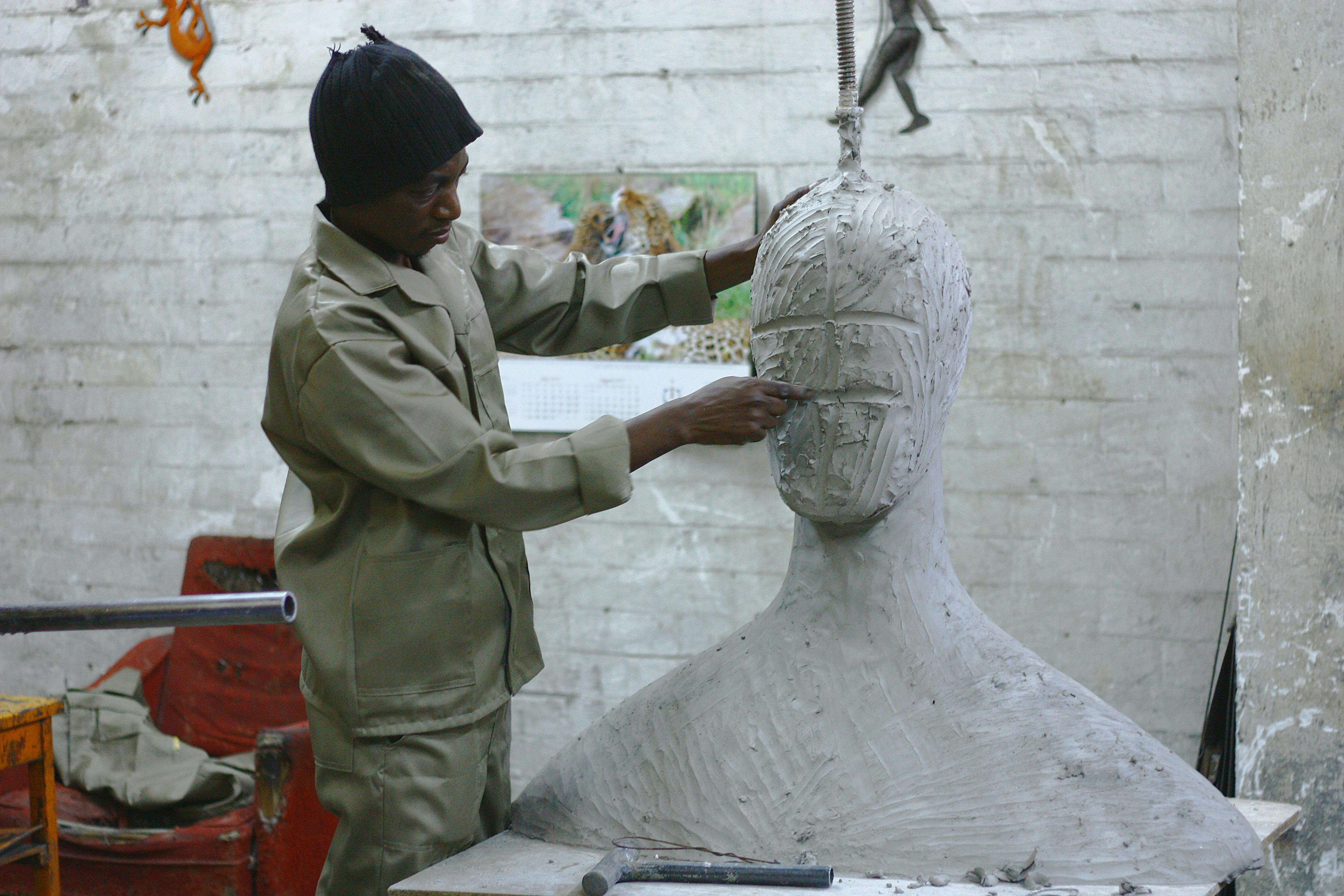 a sculptor in a studio working on a large clay bust of a human with no features yet