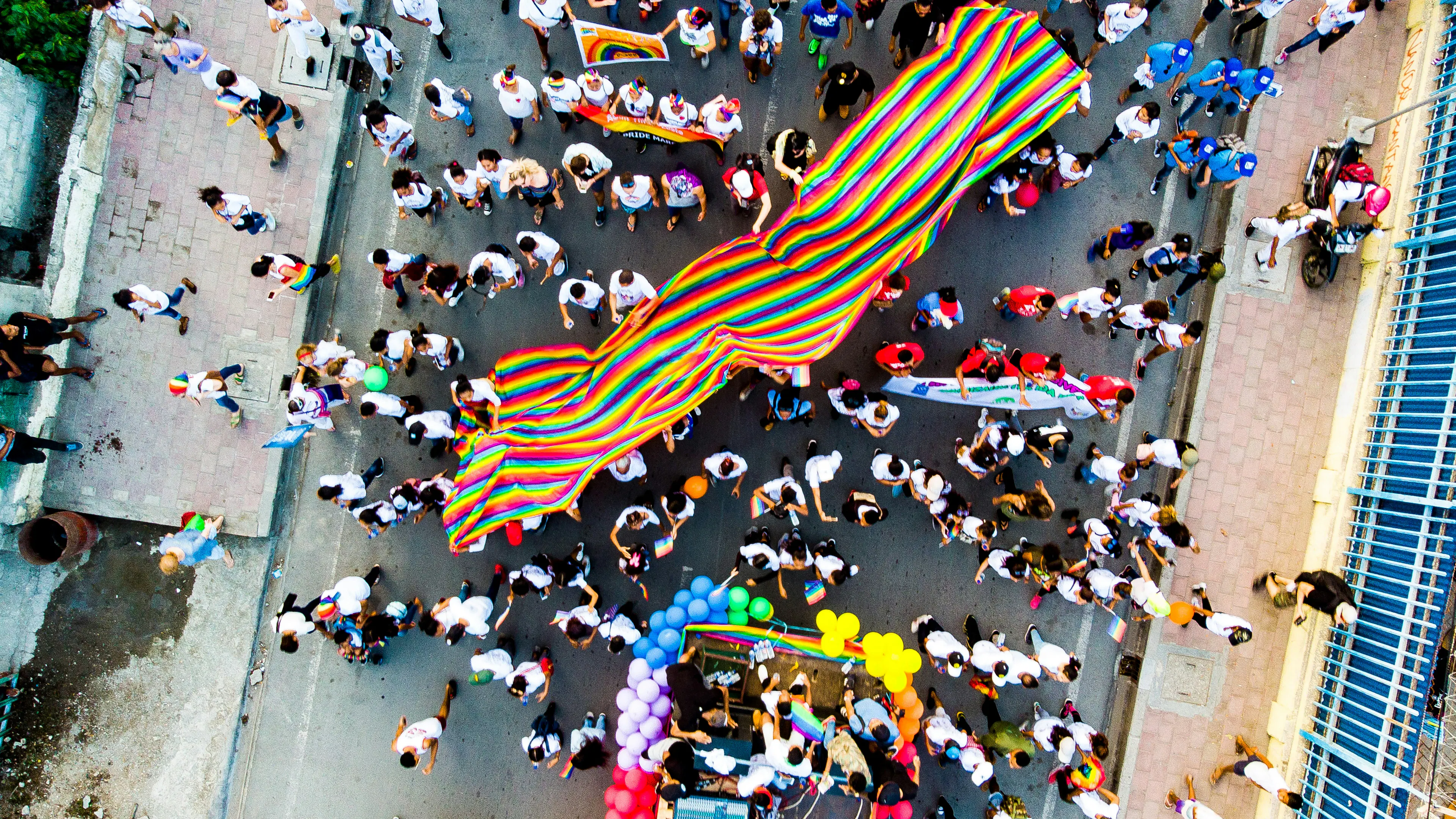 An overhead view of a street parade and a big colorful striped flag being carried in the middle
