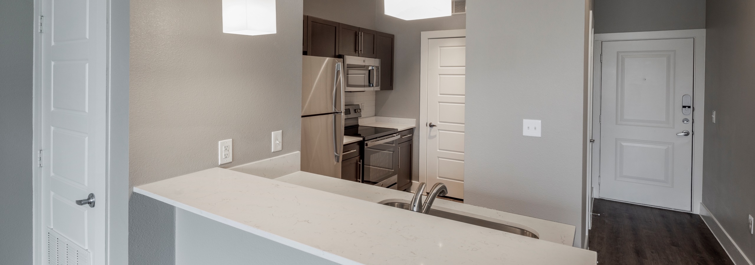 Kitchen at AMLI South Shore apartments with white quartz countertops and dark wood cabinets and floors and light gray walls