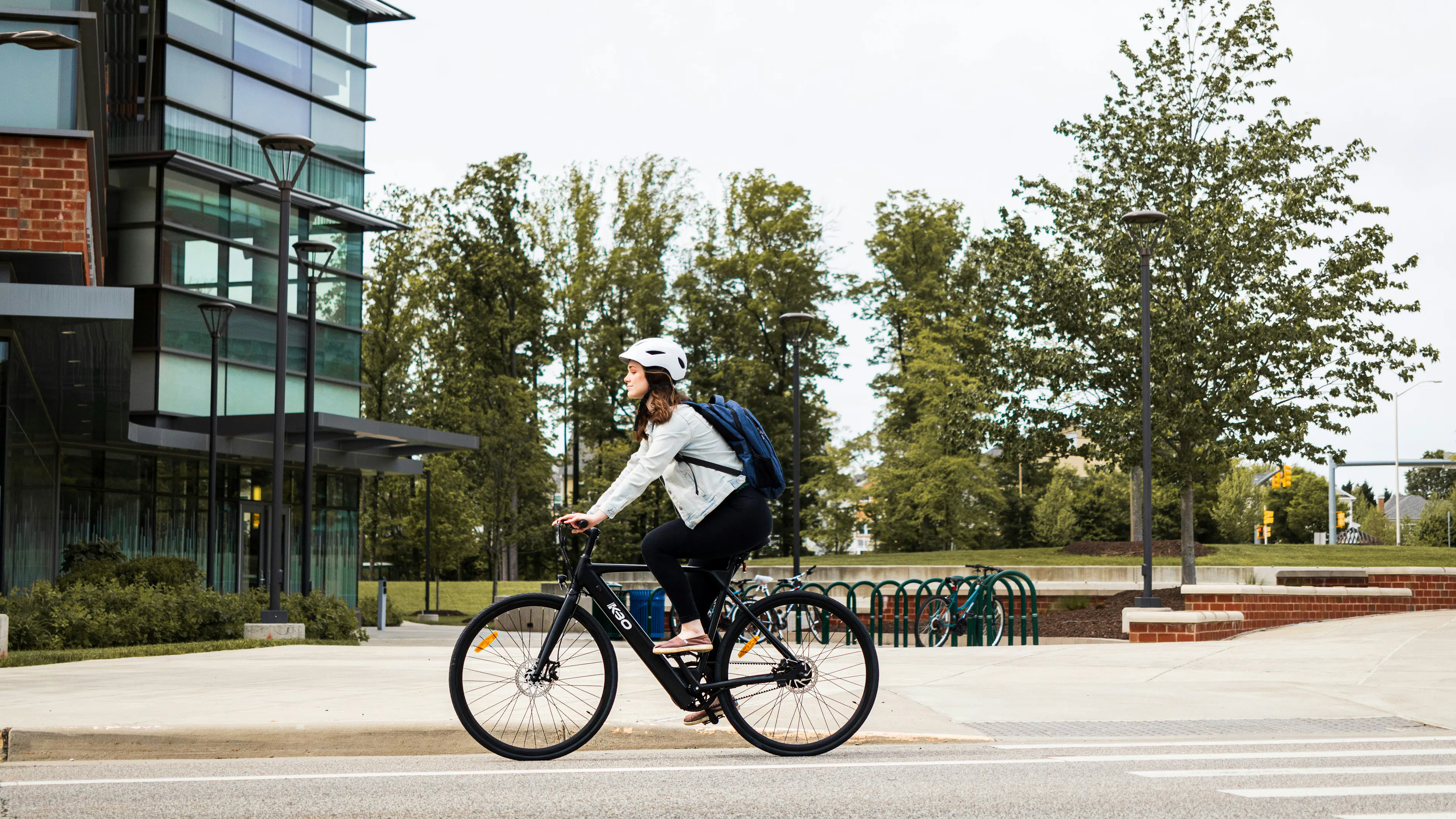 A woman on a bike with a backpack and helmet riding through a business district