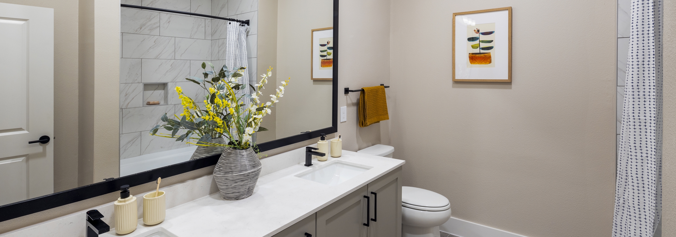 Interior view of a bathroom at AMLI North Park with a dual-sink vanity, black fixtures, a large mirror, and a white-tiled bathtub