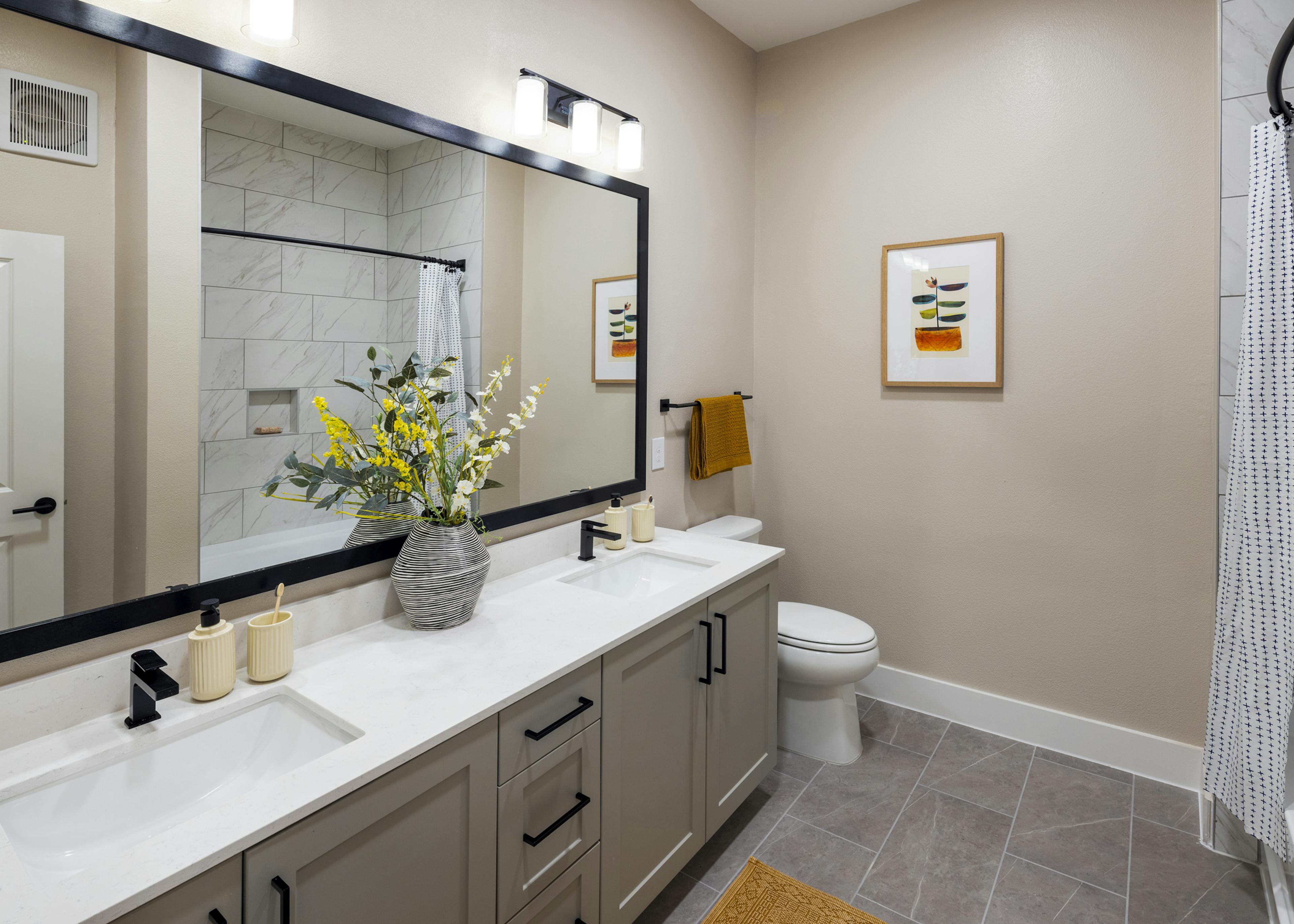 Interior view of a bathroom at AMLI North Park with a dual-sink vanity, black fixtures, a large mirror, and a white-tiled bathtub