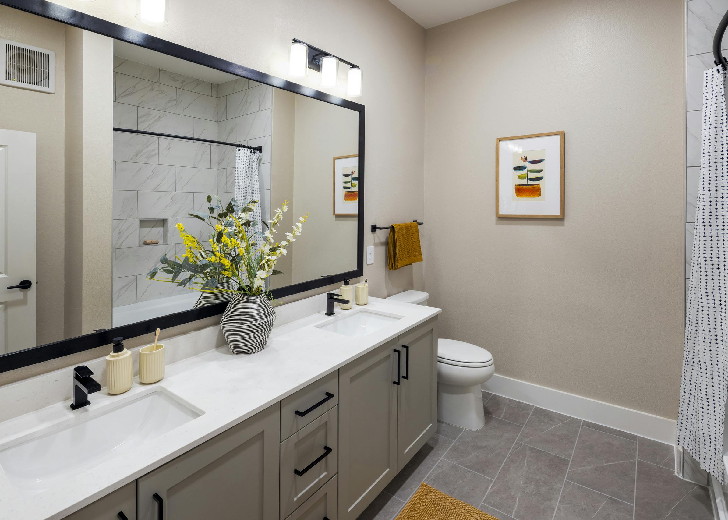 Interior view of a bathroom at AMLI North Park with a dual-sink vanity, black fixtures, a large mirror, and a white-tiled bathtub