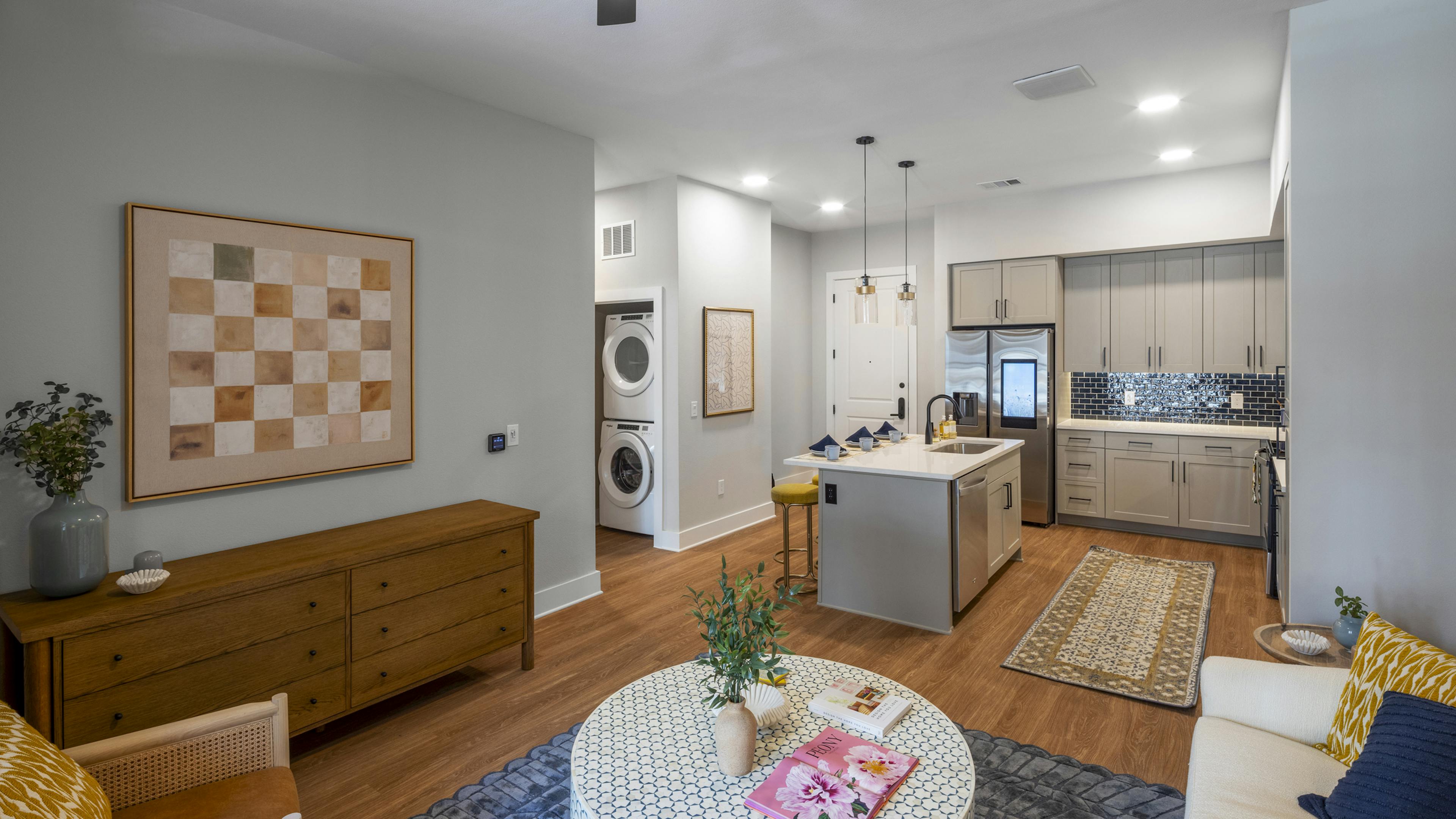 Interior view of an open-concept living area at AMLI North Park with a modern kitchen with a blue tile backsplash, and in-unit laundry