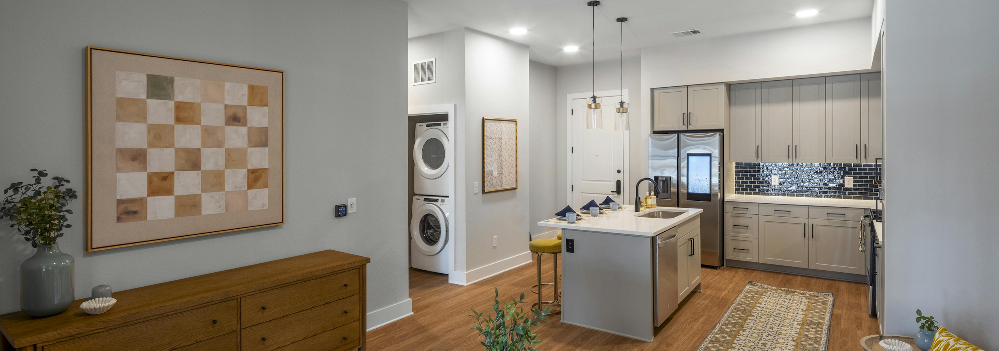 Interior view of an open-concept living area at AMLI North Park with a modern kitchen with a blue tile backsplash, and in-unit laundry