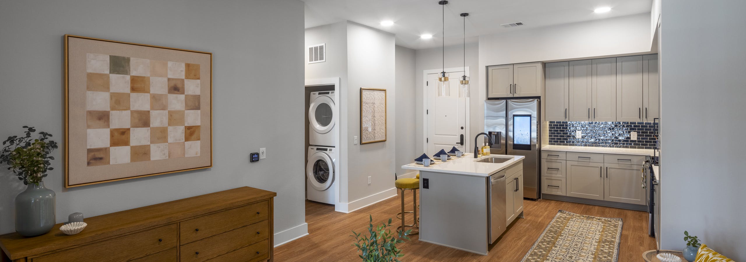 Interior view of an open-concept living area at AMLI North Park with a modern kitchen with a blue tile backsplash, and in-unit laundry