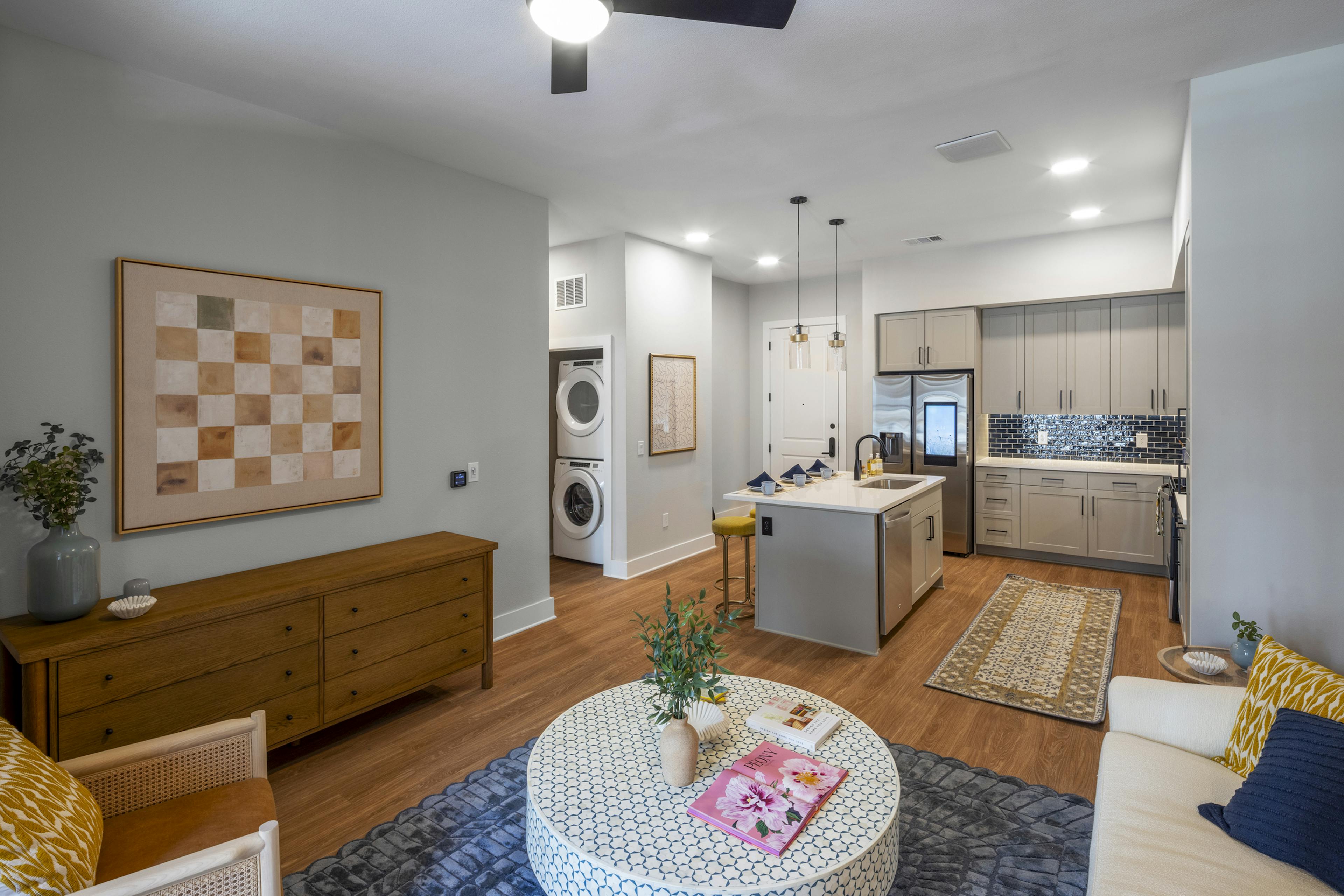 Interior view of an open-concept living area at AMLI North Park with a modern kitchen with a blue tile backsplash, and in-unit laundry