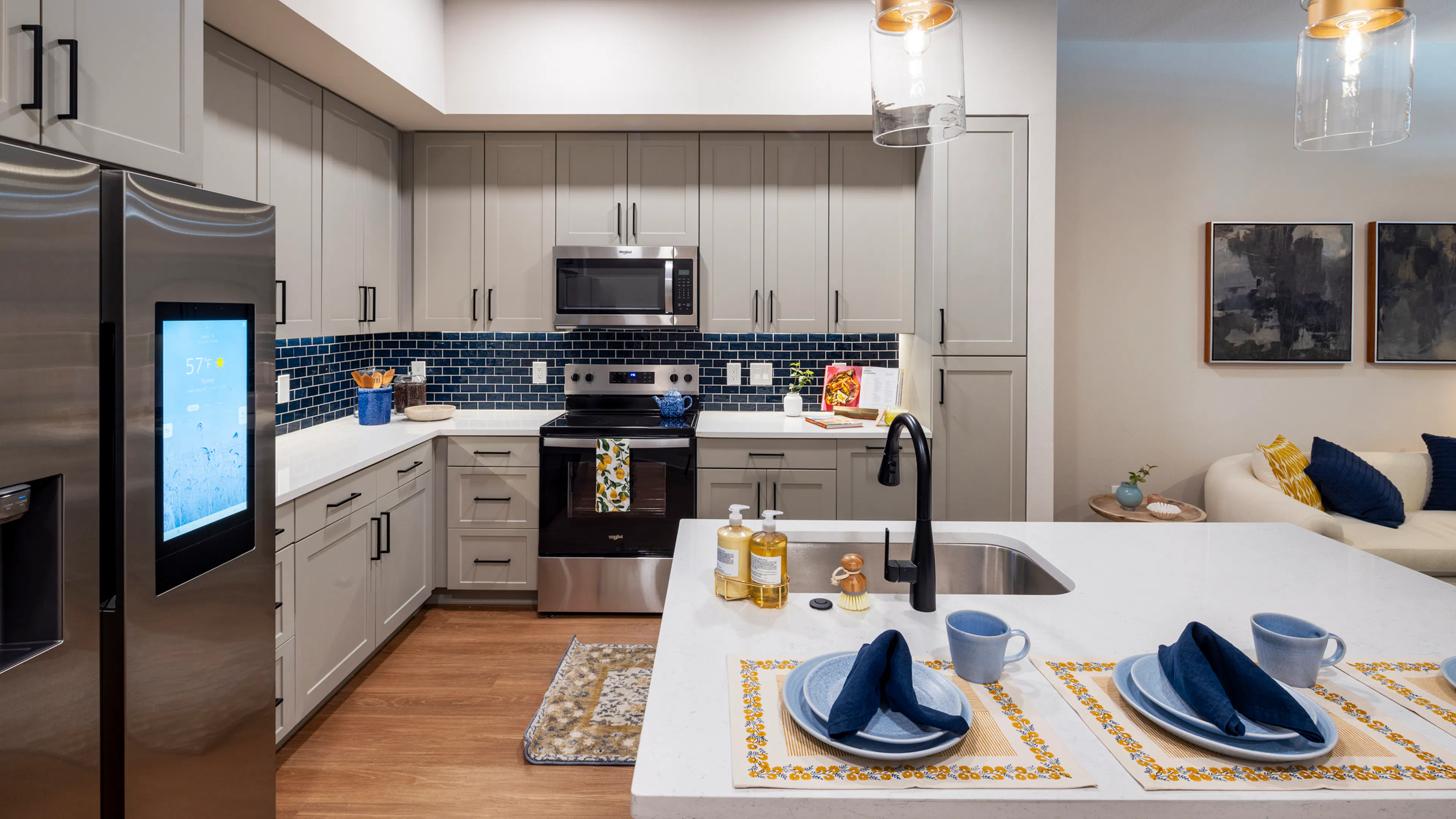 Interior view of a kitchen at AMLI North Park apartments with gray cabinets, a blue tile backsplash, stainless steel appliances, and pendant lighting