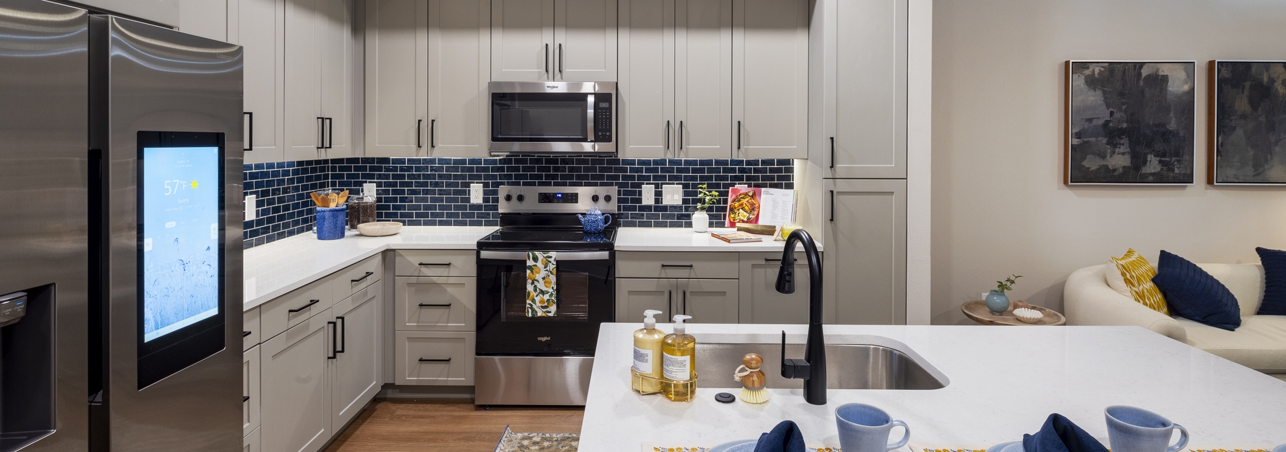 Interior view of a kitchen at AMLI North Park apartments with gray cabinets, a blue tile backsplash, stainless steel appliances, and pendant lighting