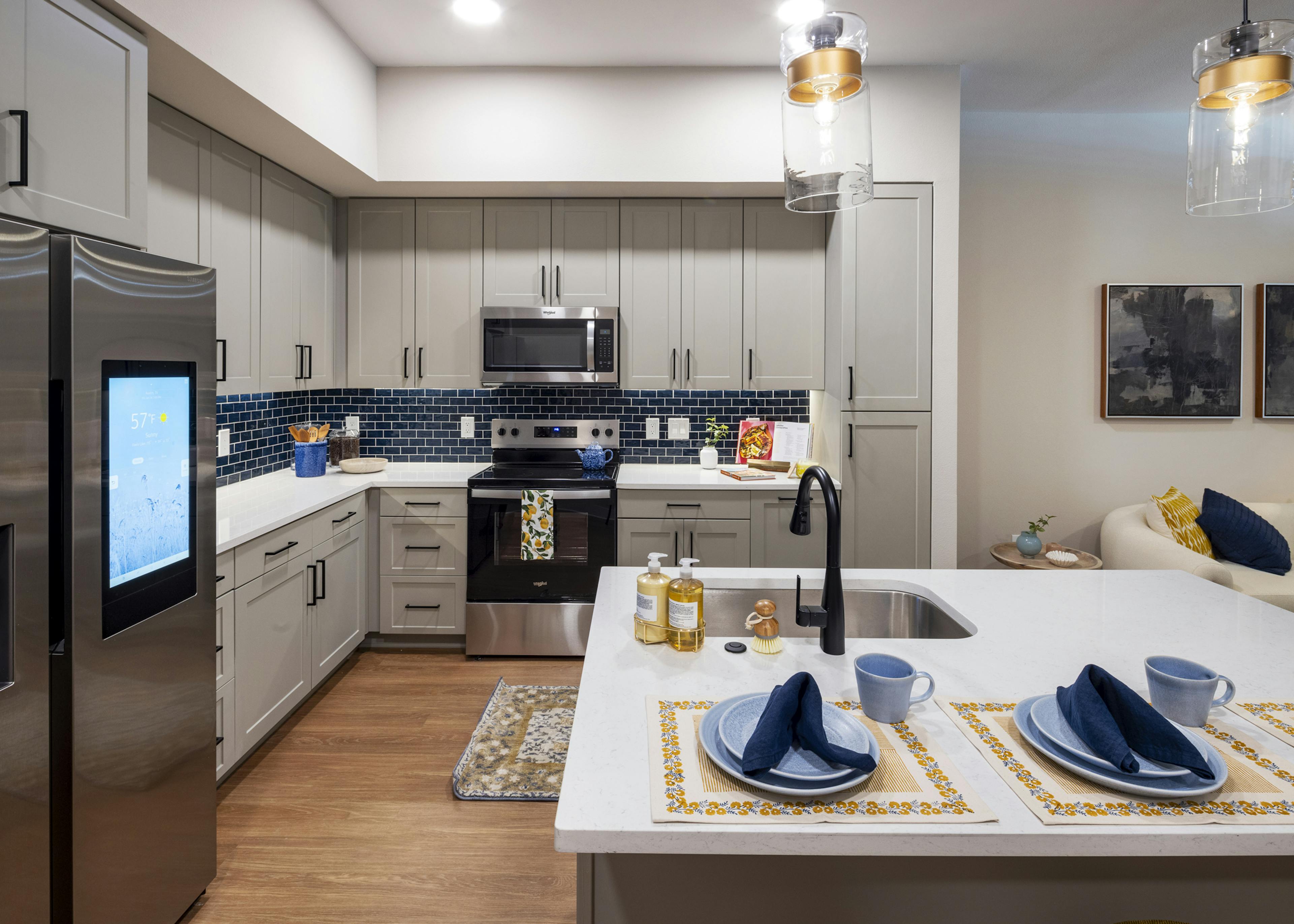 Interior view of a kitchen at AMLI North Park apartments with gray cabinets, a blue tile backsplash, stainless steel appliances, and pendant lighting