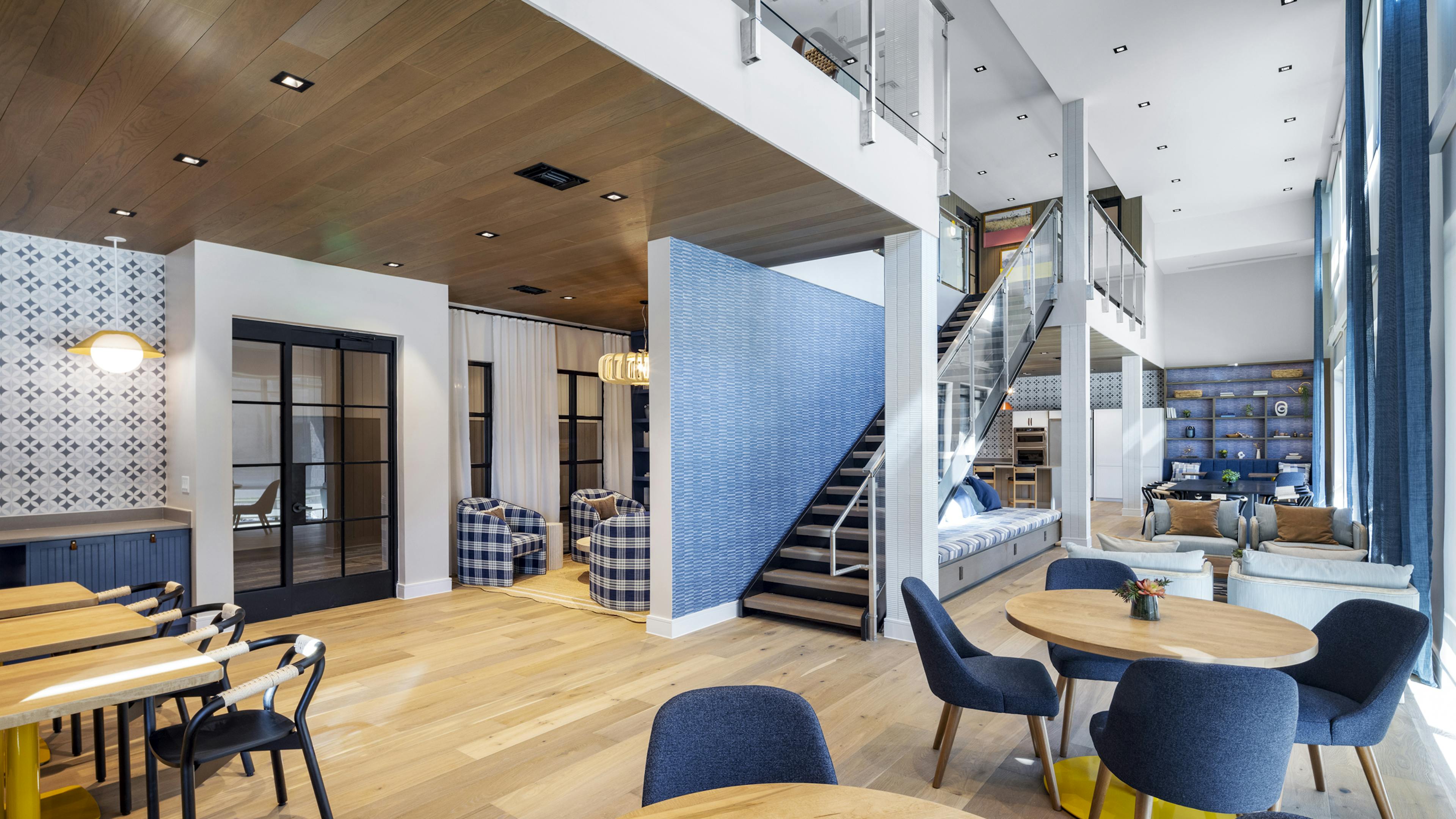 Spacious clubhouse at AMLI North Park with open seating, modern lighting, a staircase with glass railing, and high ceilings