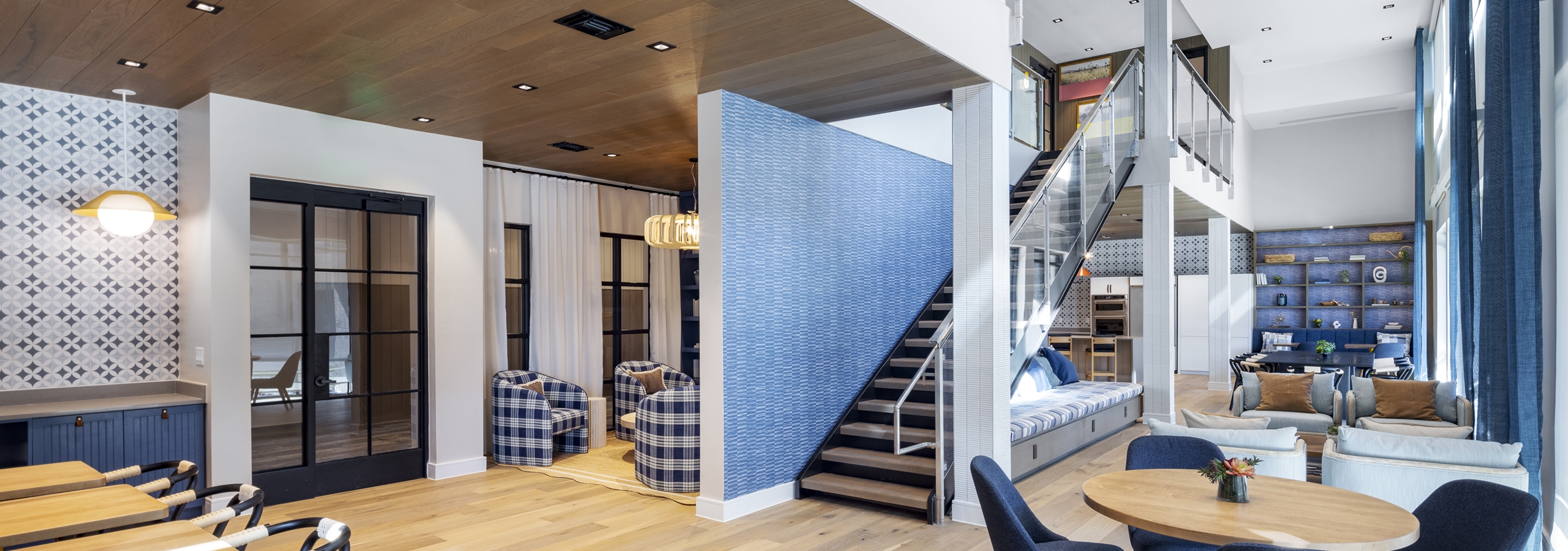 Spacious clubhouse at AMLI North Park with open seating, modern lighting, a staircase with glass railing, and high ceilings