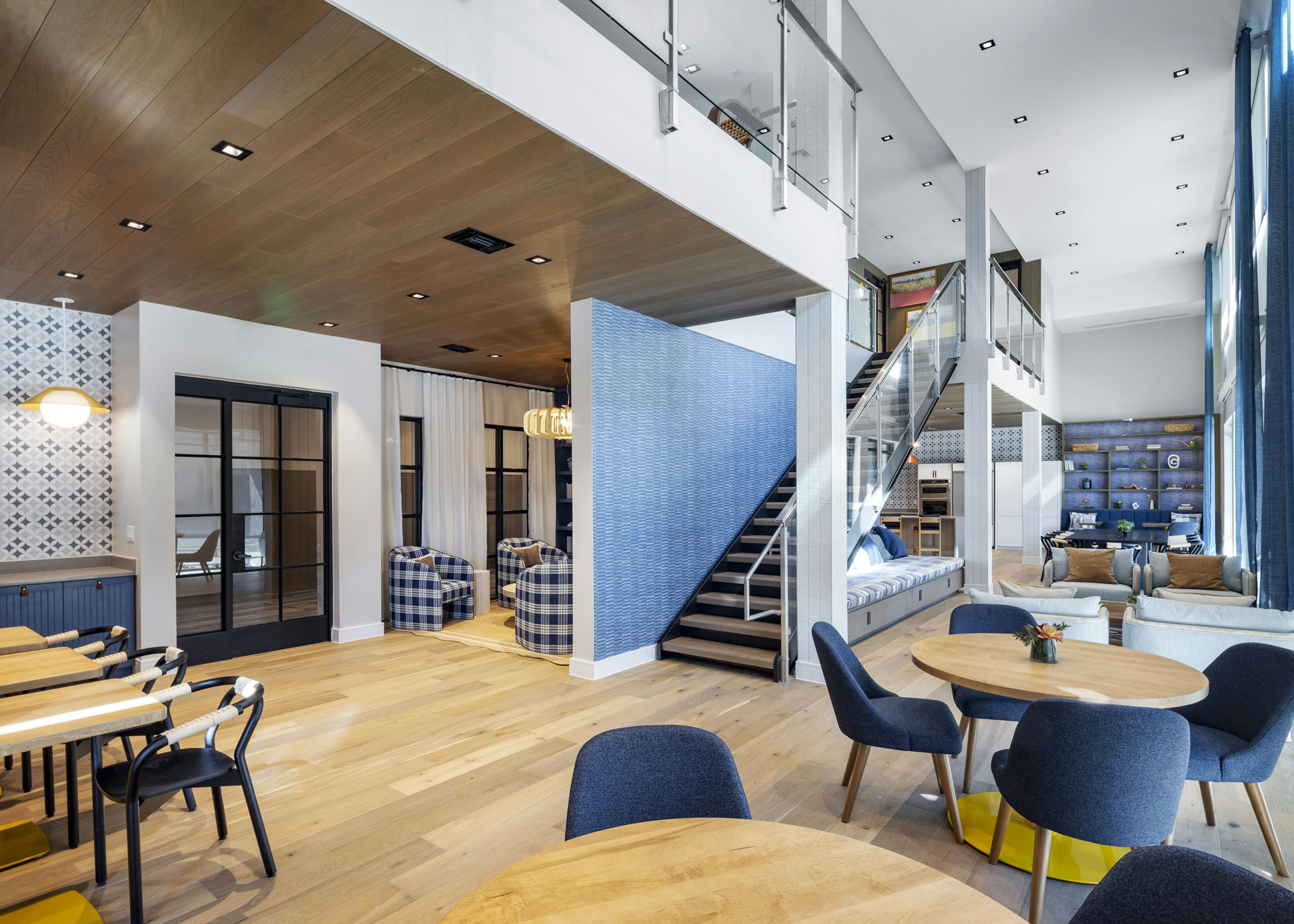 Spacious clubhouse at AMLI North Park with open seating, modern lighting, a staircase with glass railing, and high ceilings