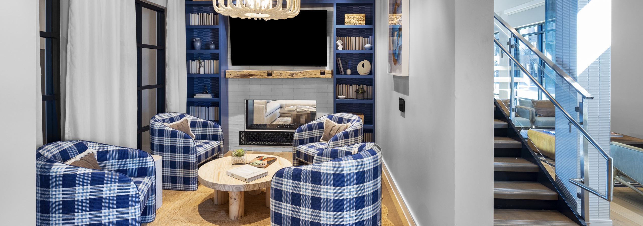 Lounge area at AMLI North Park community with plaid armchairs, a wooden coffee table, a built-in fireplace, and a TV on a blue accent wall