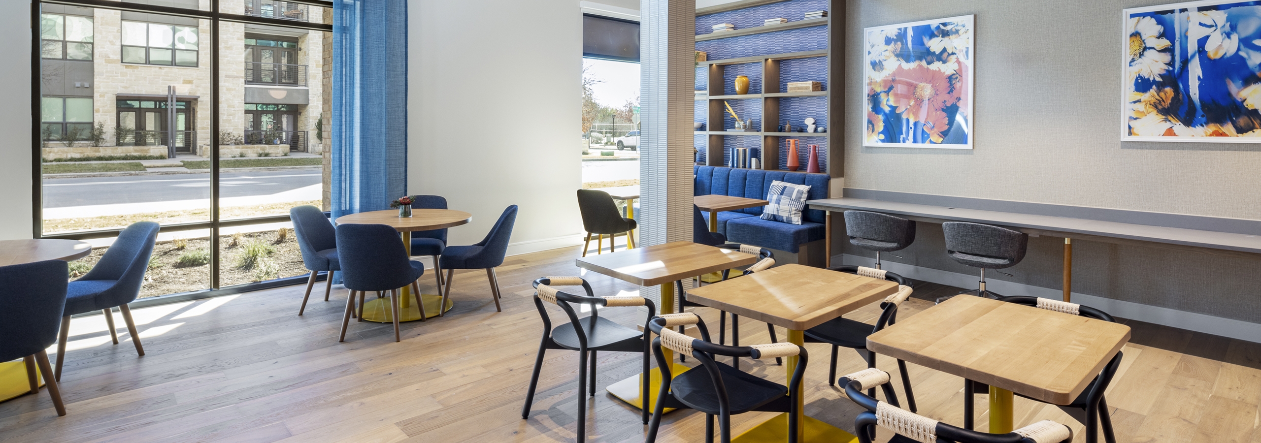 Coworking space at AMLI North Park apartments with natural light, wood tables, navy chairs, and a built-in bookshelf with decorative accents