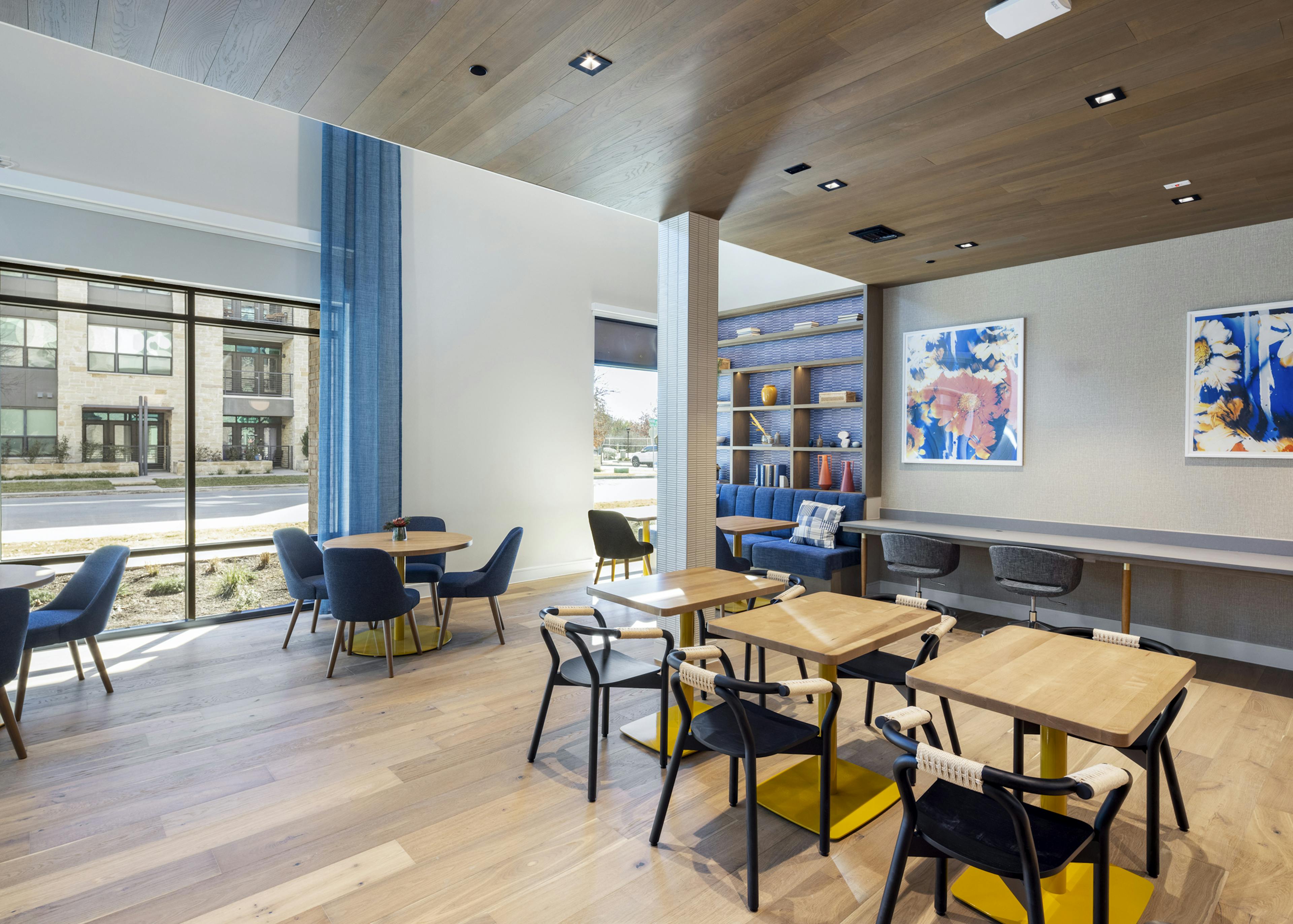 Coworking space at AMLI North Park apartments with natural light, wood tables, navy chairs, and a built-in bookshelf with decorative accents