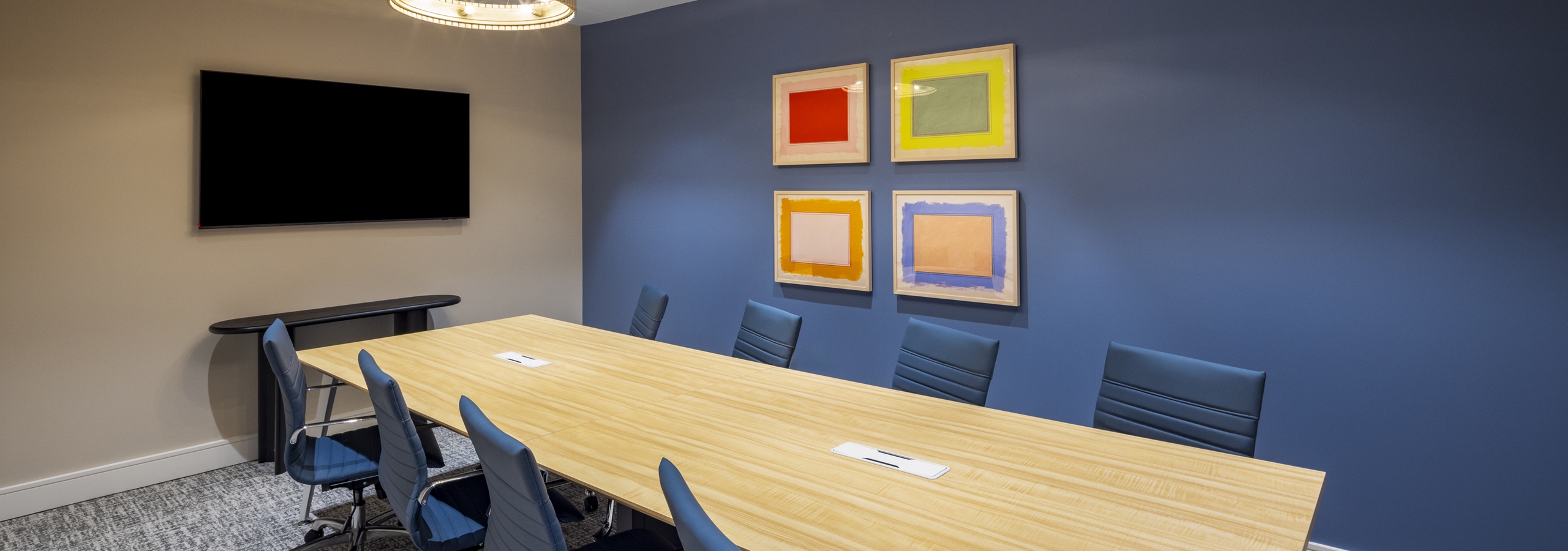 Conference room at AMLI North Park apartments with a long wooden table, blue accent wall, modern chandeliers, and colorful abstract artwork