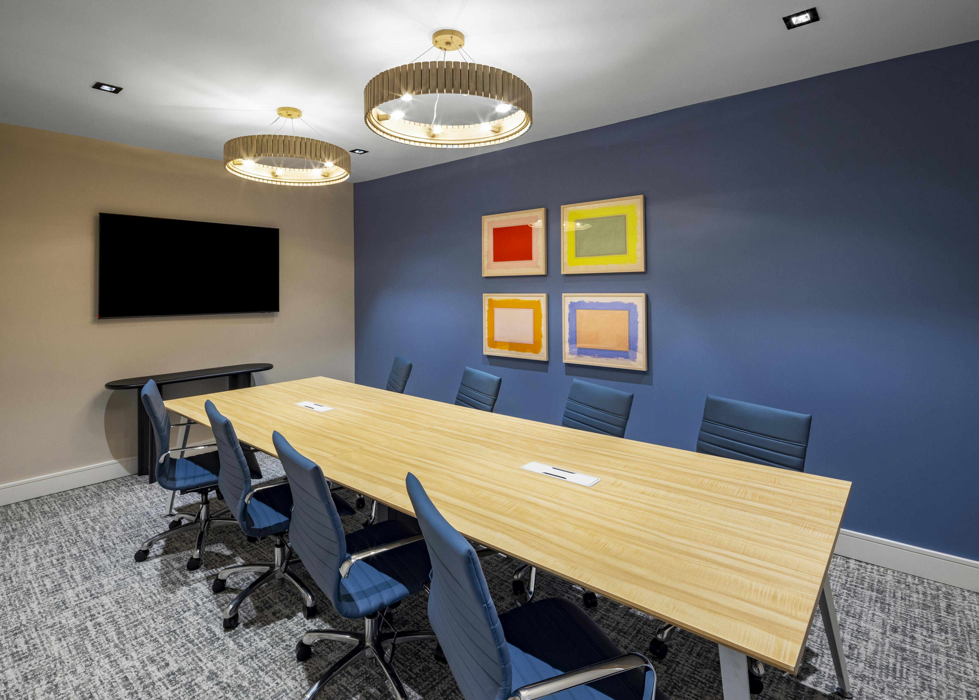 Conference room at AMLI North Park apartments with a long wooden table, blue accent wall, modern chandeliers, and colorful abstract artwork
