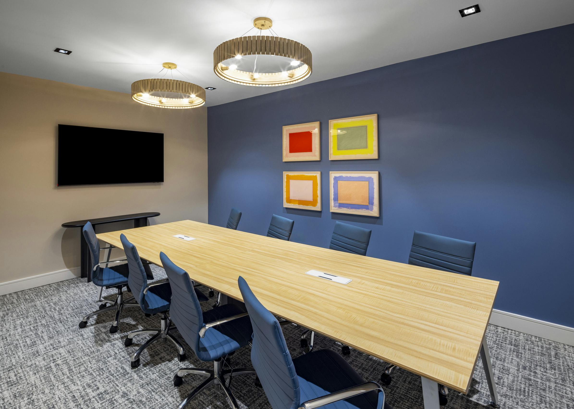 Conference room at AMLI North Park apartments with a long wooden table, blue accent wall, modern chandeliers, and colorful abstract artwork