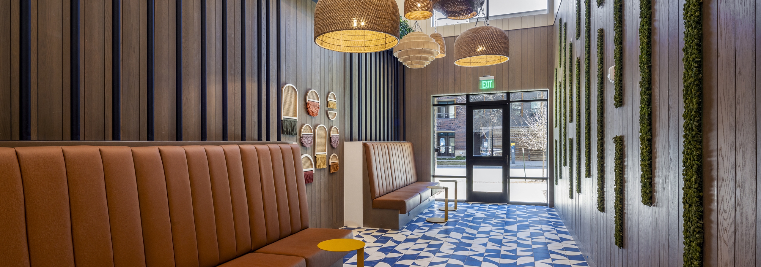 Coworking area at AMLI North Park community with leather bench seating, woven pendant lights, bold blue tile flooring, and decorative wall greenery