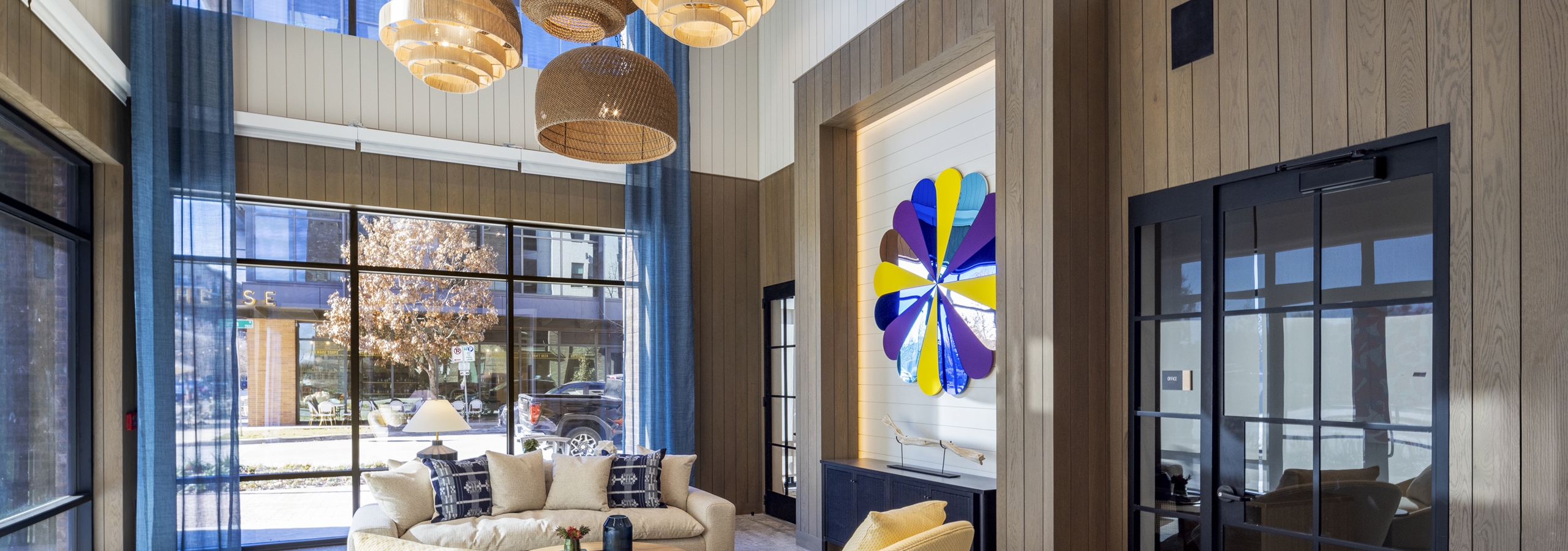 Lobby at AMLI North Park apartments with woven pendant lights, plush seating, floor-to-ceiling windows, and a colorful wall flower