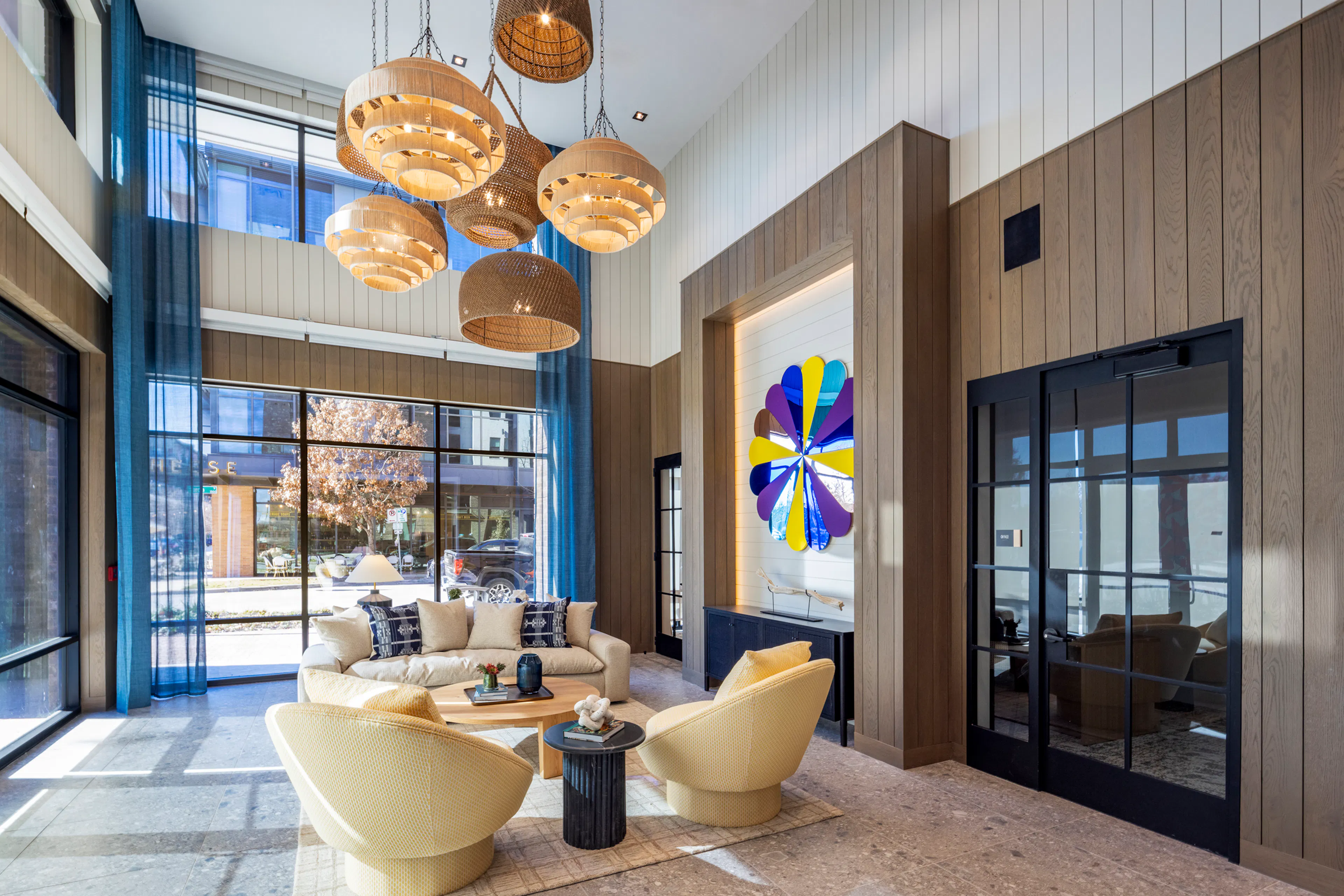Lobby at AMLI North Park apartments with woven pendant lights, plush seating, floor-to-ceiling windows, and a colorful wall flower
